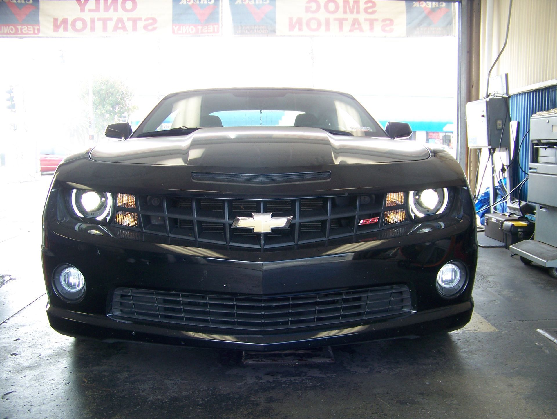 Front view of a black Chevrolet Camaro in a garage, headlights on