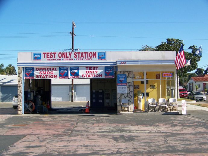 Small roadside test-only station with open bays, signs, and an American flag under a clear blue sky