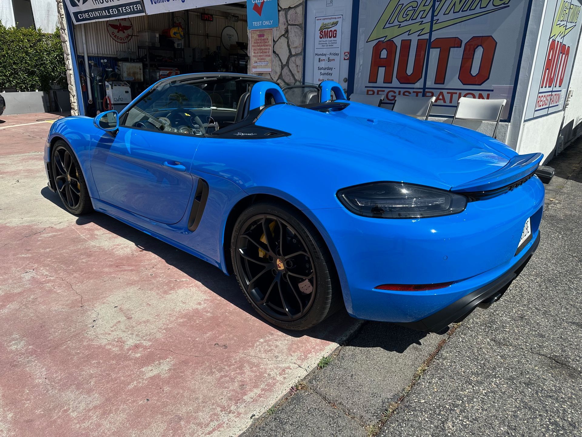 Blue sports car parked outside an auto shop, angled front-left view.