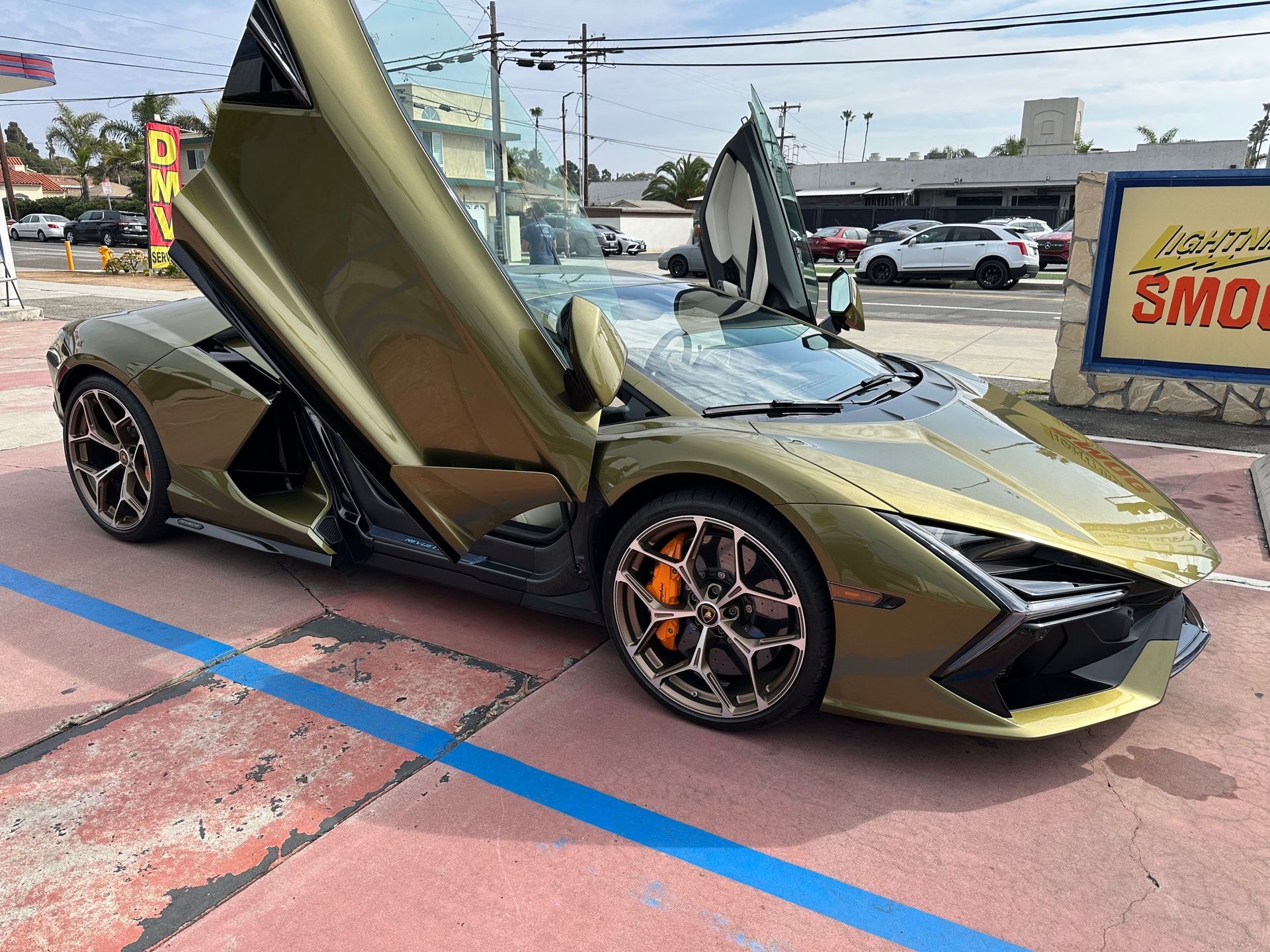 Gold Lamborghini with scissor doors open in a parking lot, viewed from the front-left.