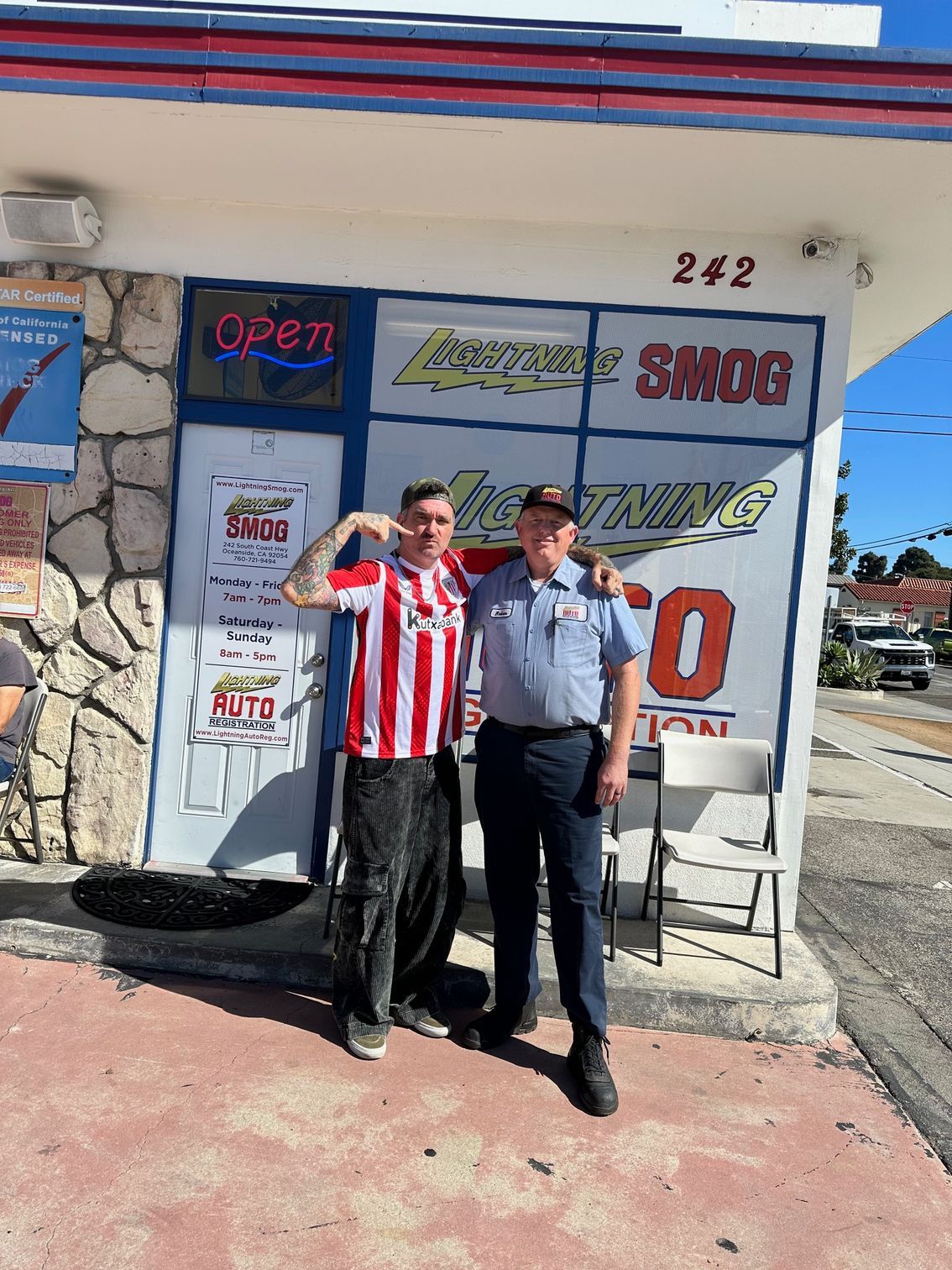 Two men standing outside a sports shop, one in a red-and-white striped jersey, one in a blue uniform.