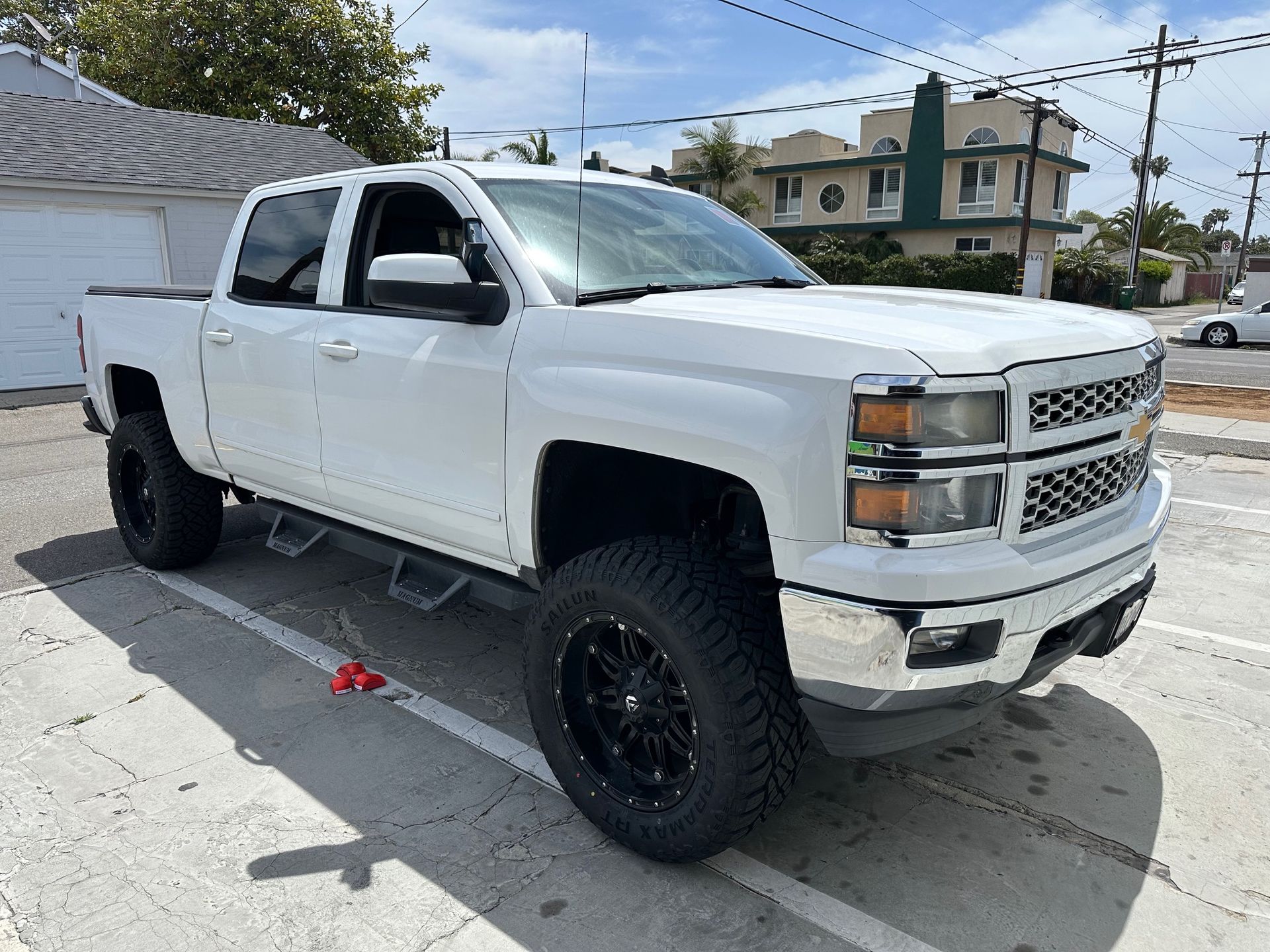 White lifted Chevrolet pickup truck parked on a street in bright daylight