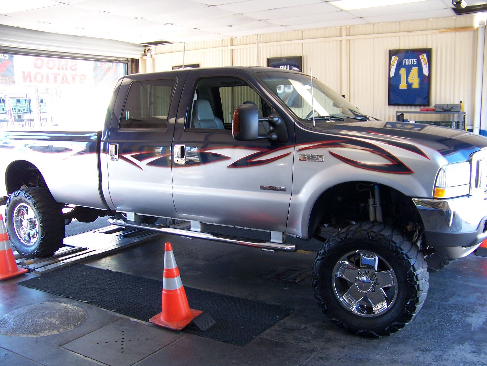 Lifted silver pickup truck on a dynamometer inside a garage, with traffic cones nearby