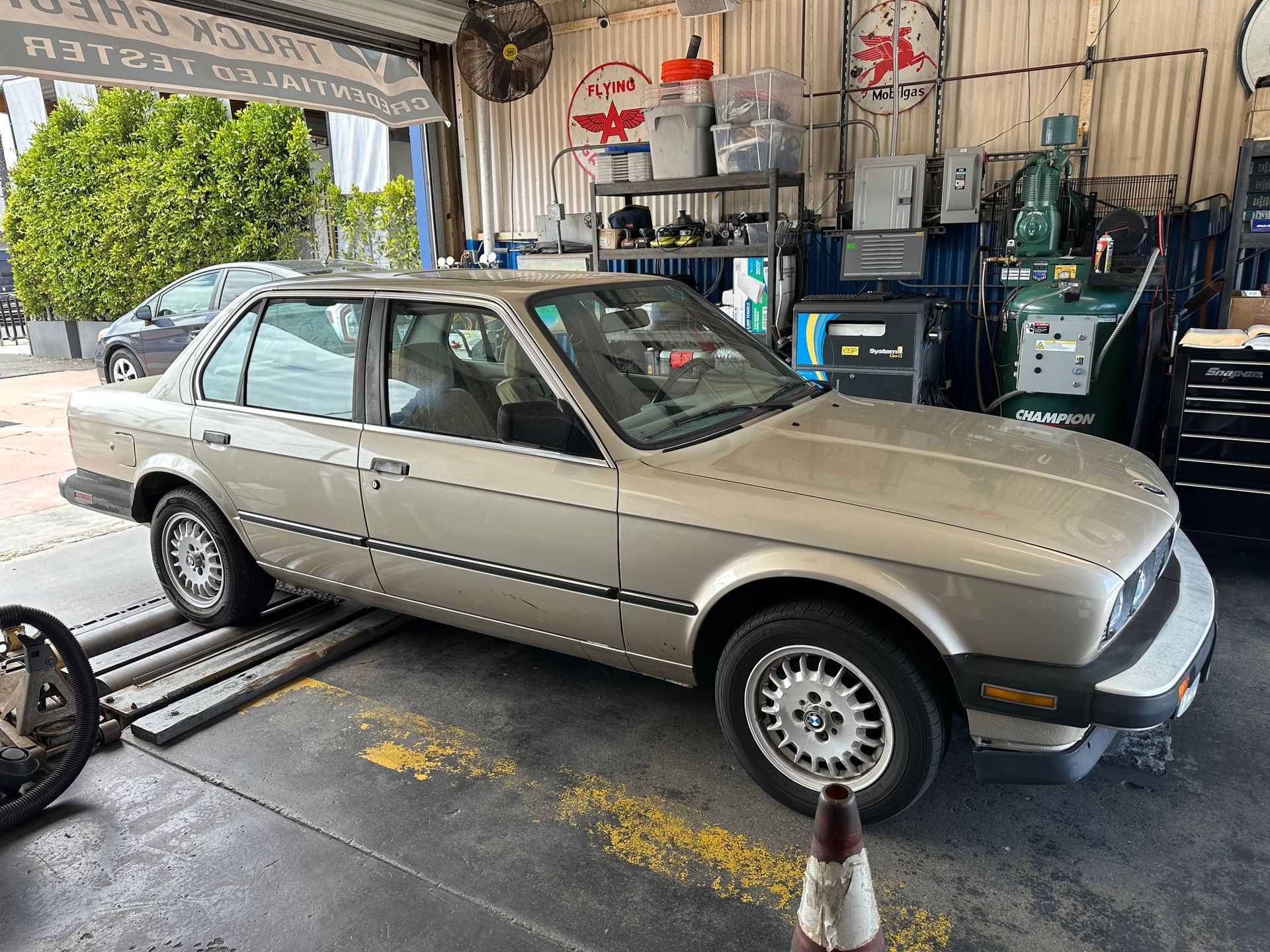 Beige sedan on a lift in an auto repair shop, with tools and equipment in the background.