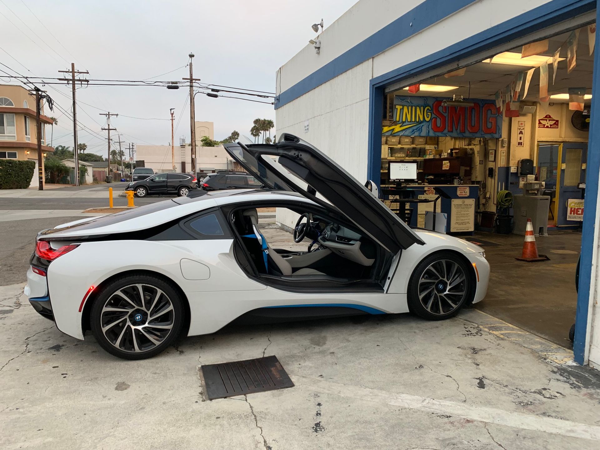 White sports car with gullwing doors open outside an auto shop at dusk