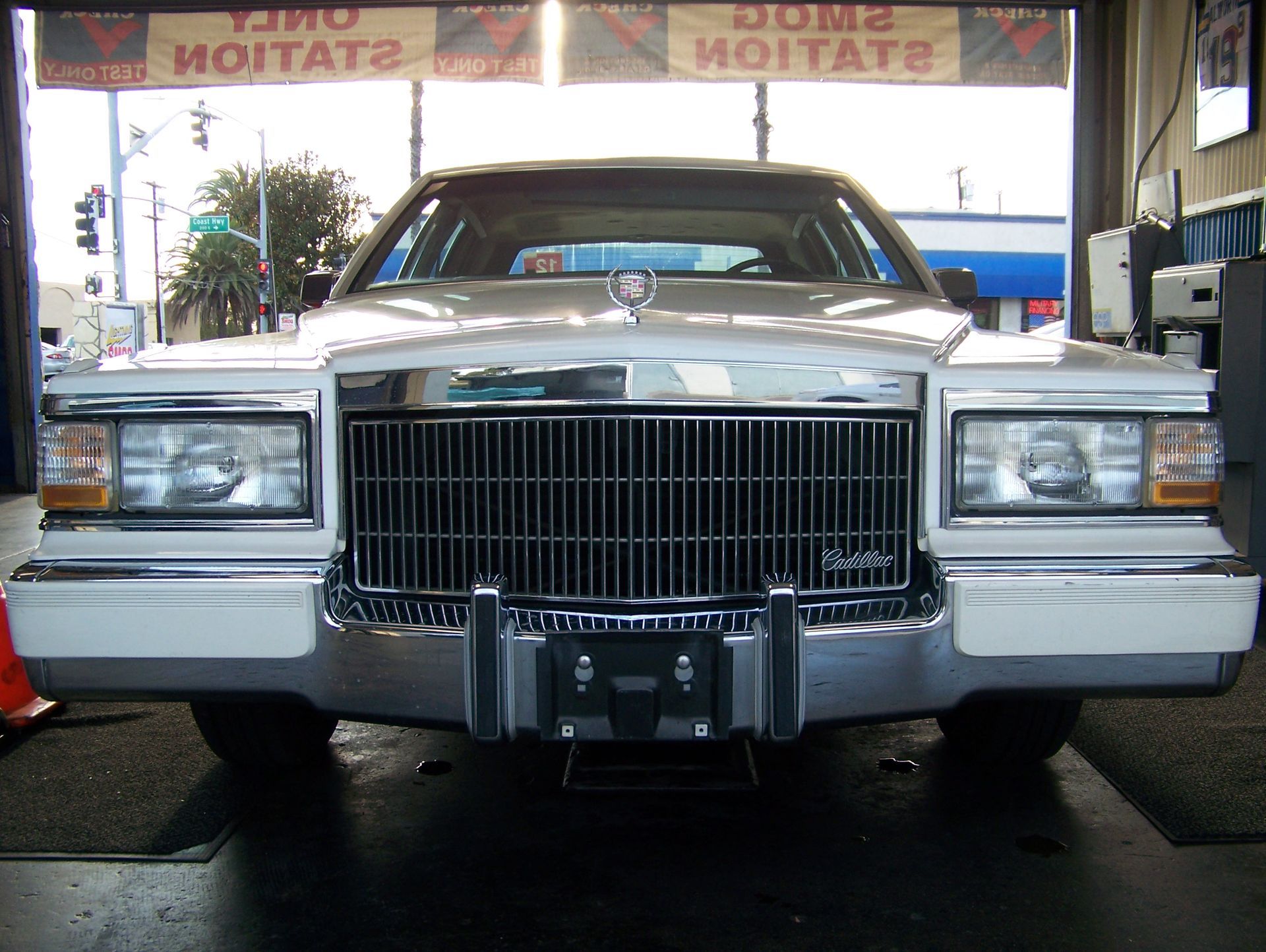 Front view of a vintage silver Cadillac at a gas station under a canopy.