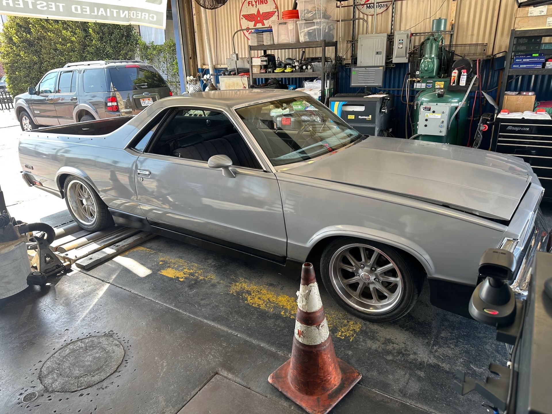 Silver classic car in an auto shop bay, with a traffic cone in front and tools in the background