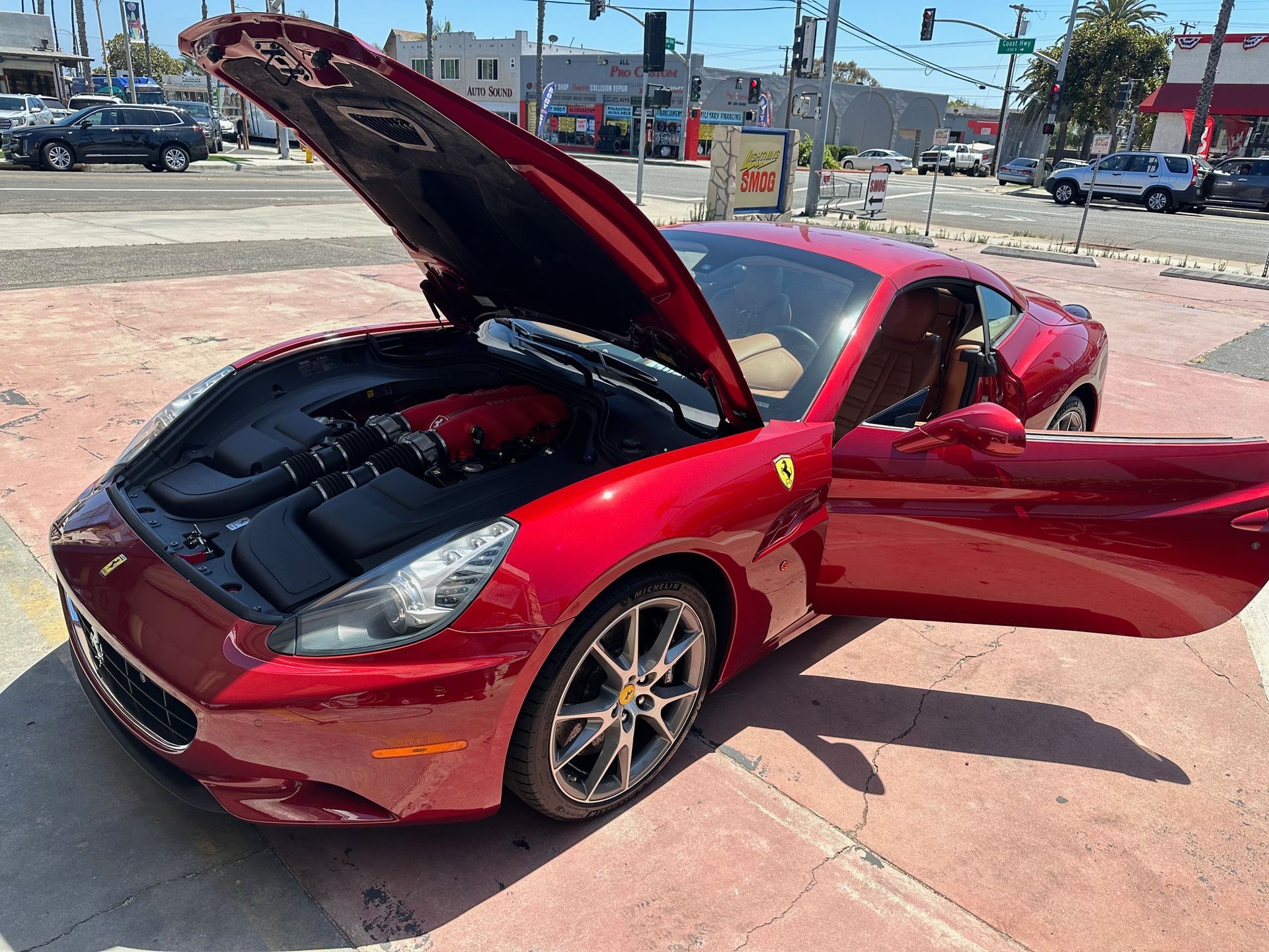Red sports car with hood and driver-side door open in a parking lot, showing the engine compartment.