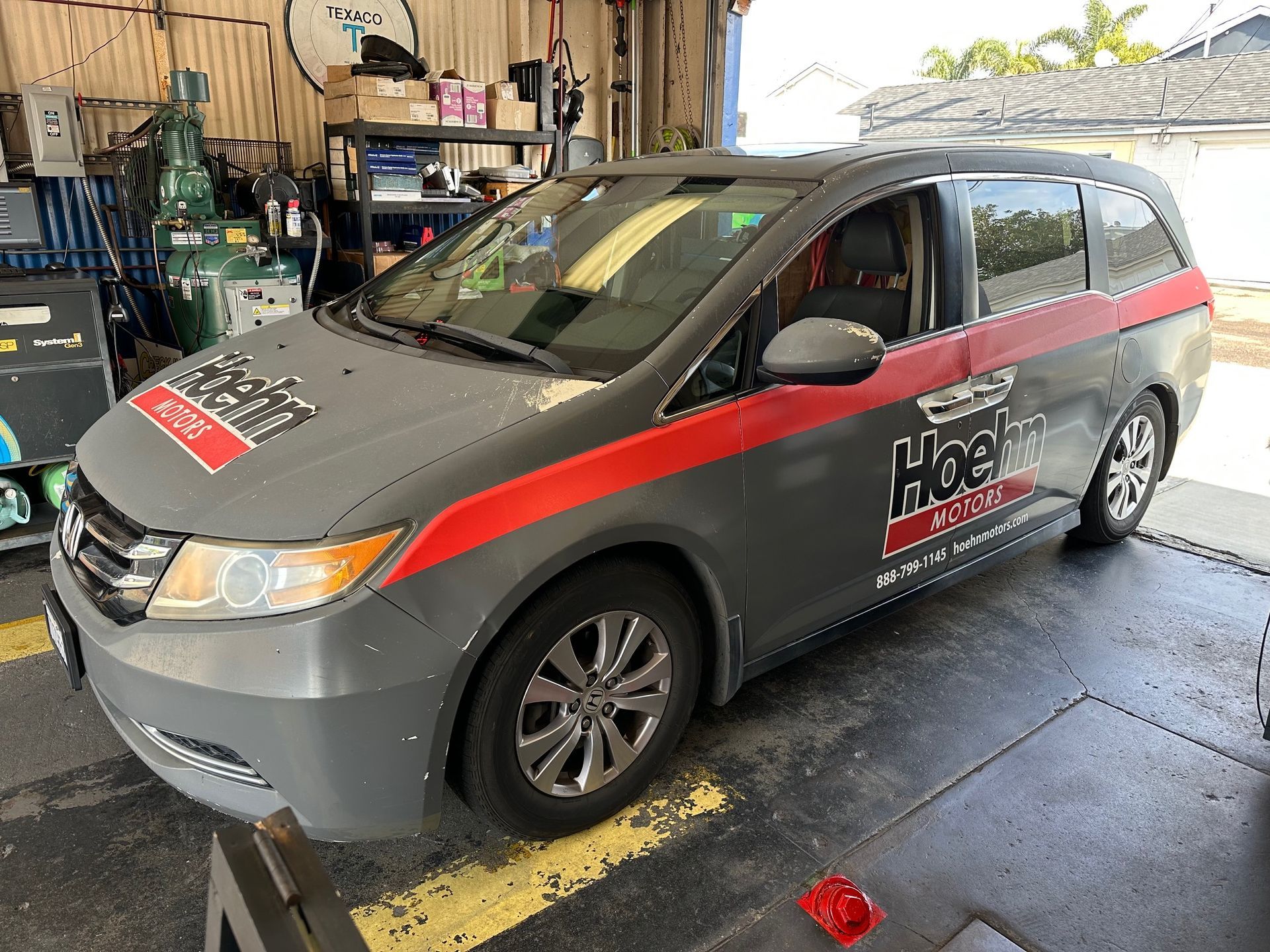 Gray and red service van parked in a garage, with tools and equipment in the background