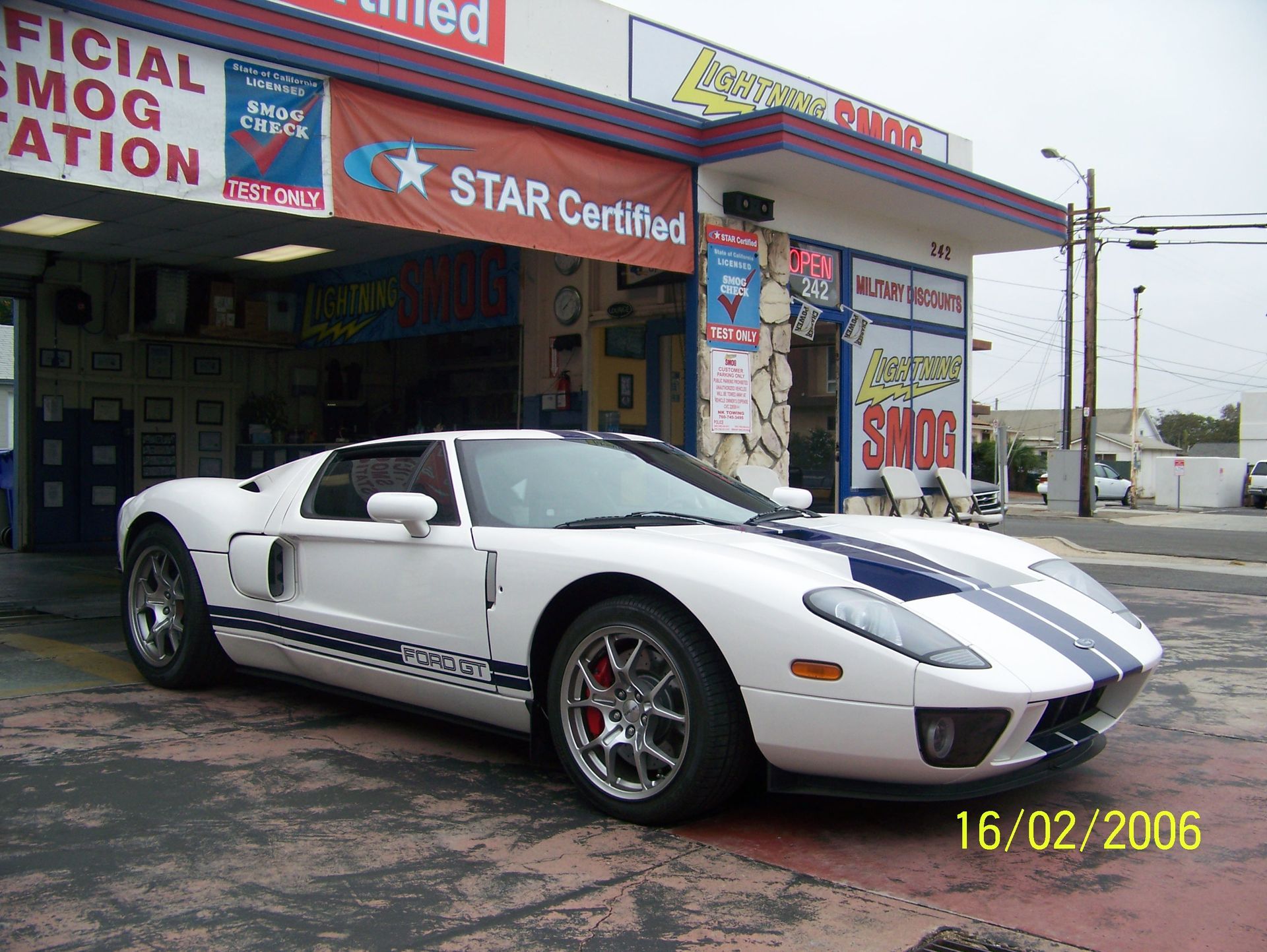 White sports car with racing stripes parked outside an auto shop