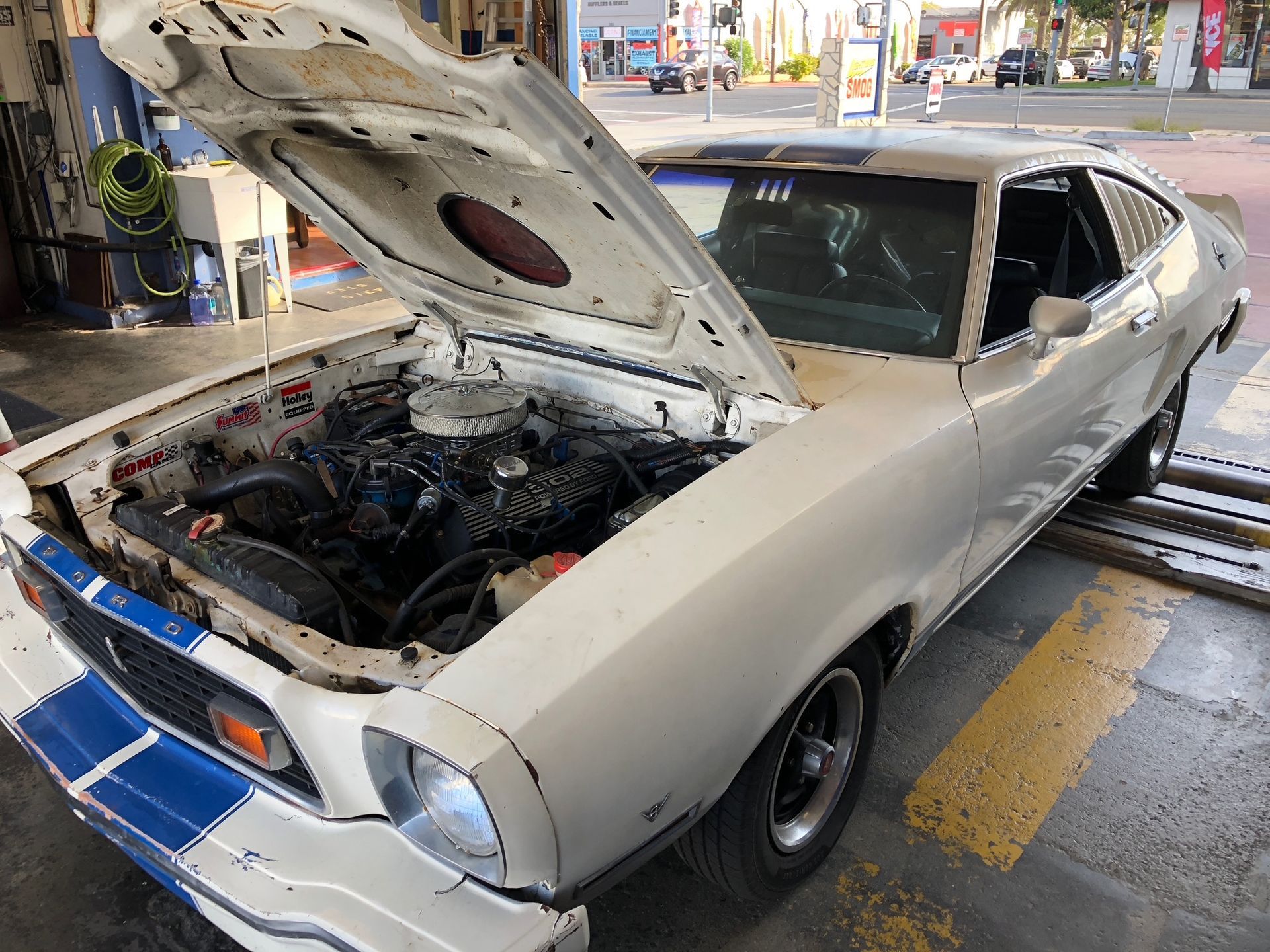 Classic white muscle car with hood open at a gas station, showing the engine.