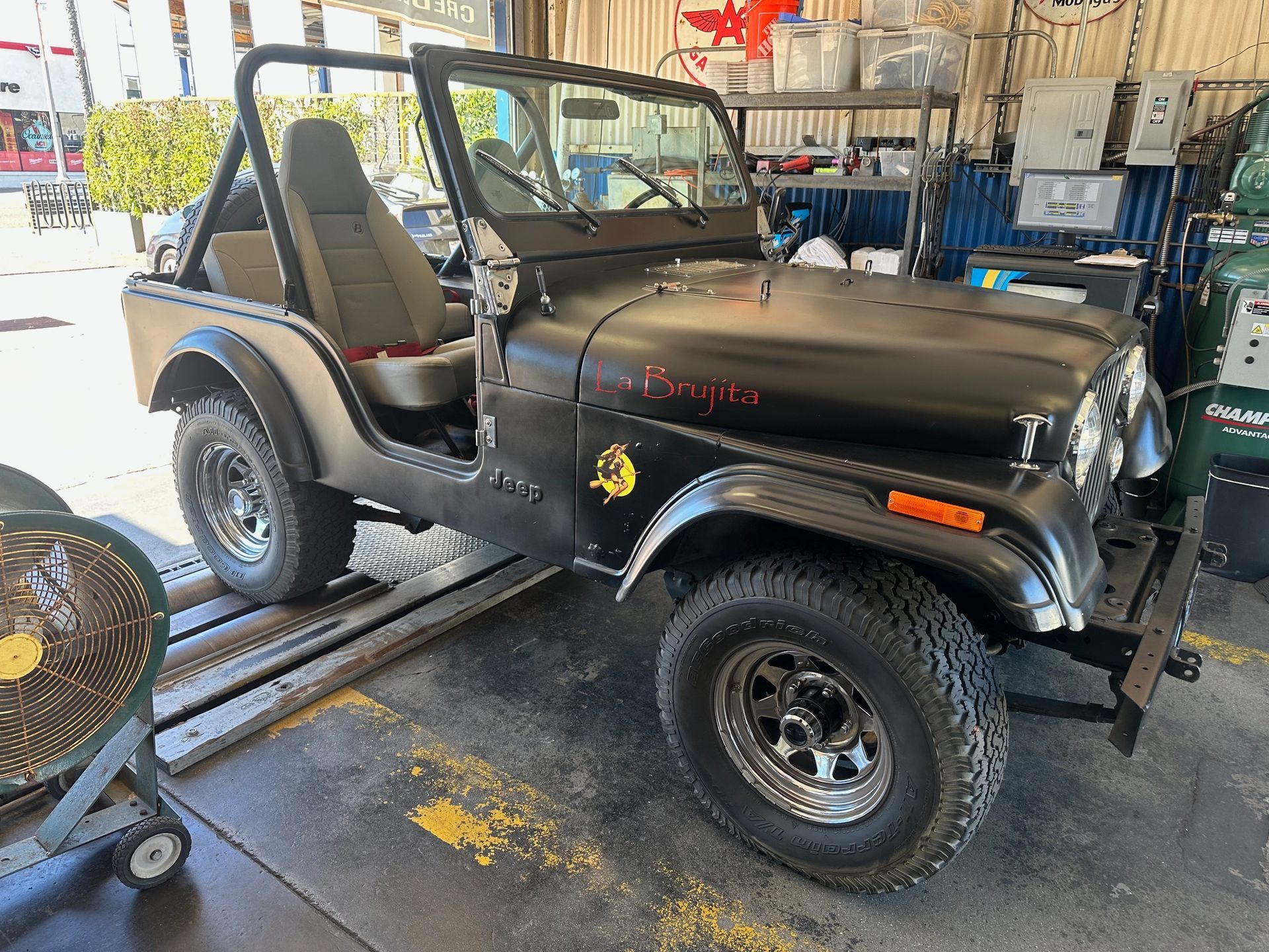 Black Jeep Wrangler in a garage, viewed from the side with the doors off and a soft top.