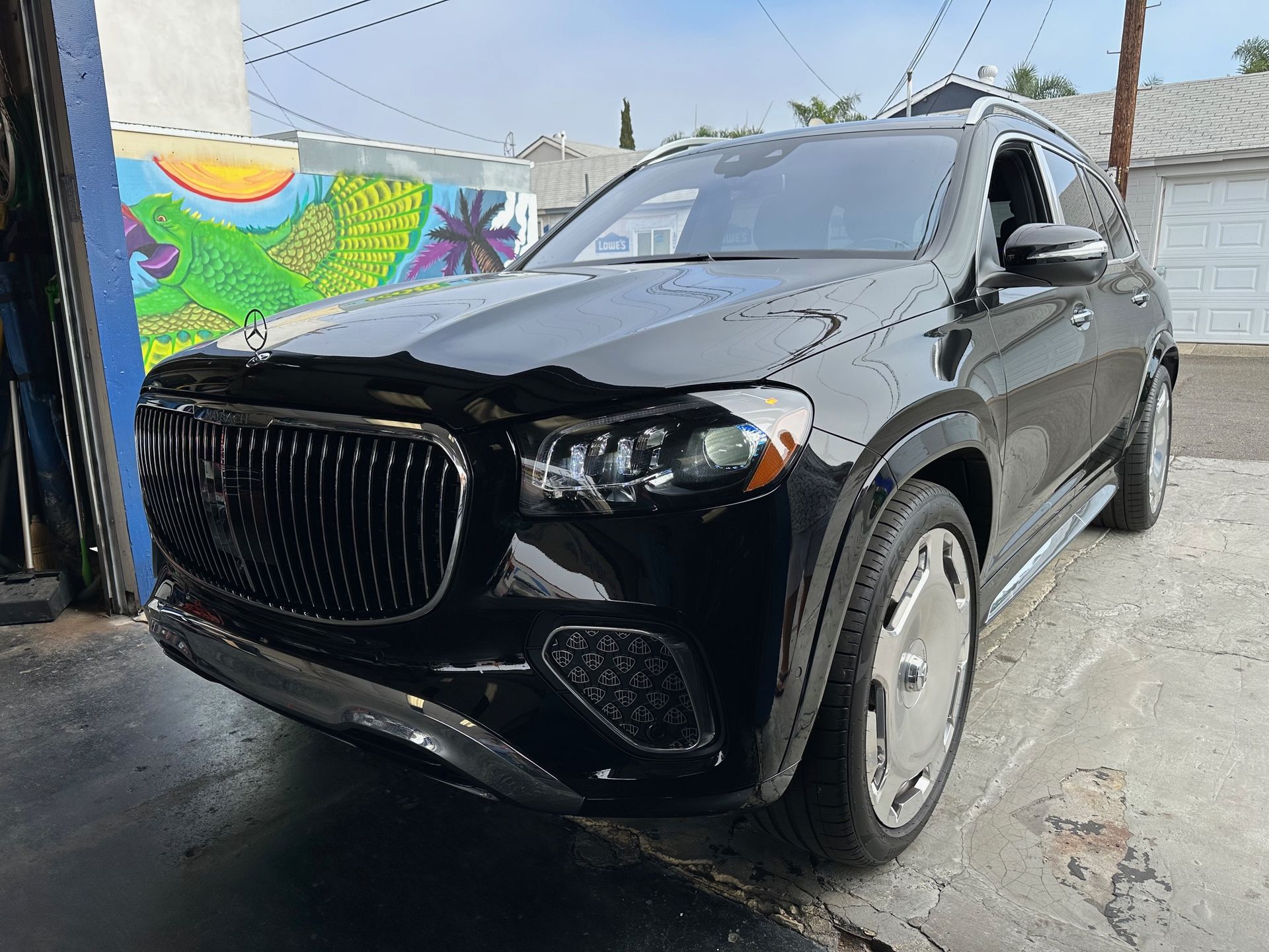 Black SUV parked in a narrow alley beside a colorful mural and utility poles.