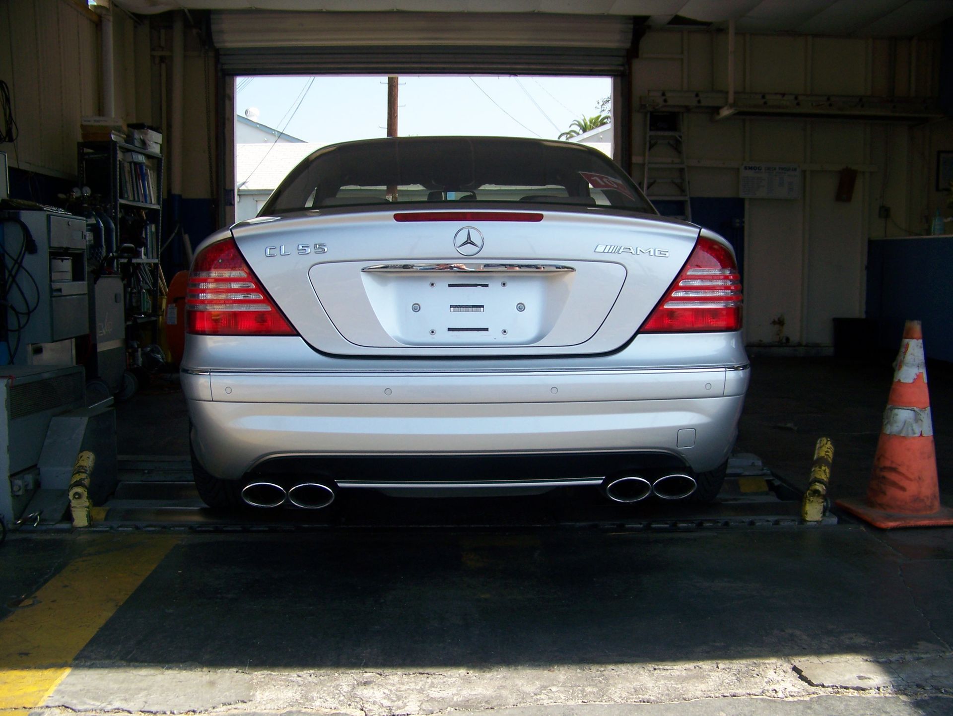 Rear view of a silver Mitsubishi sedan parked in a garage, with traffic cone and open bay door.