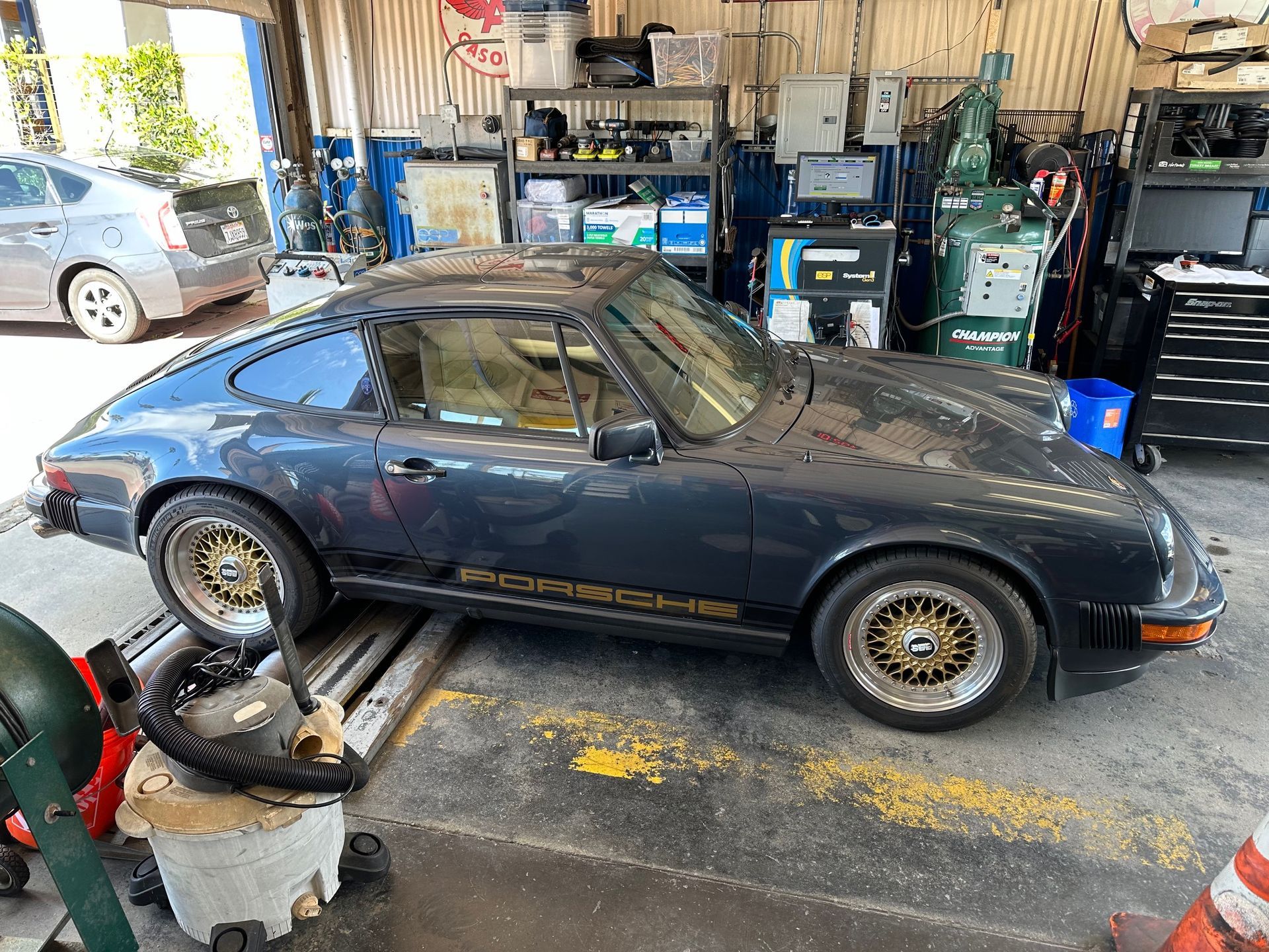 Dark blue vintage sports car in an auto workshop with tools and equipment around it
