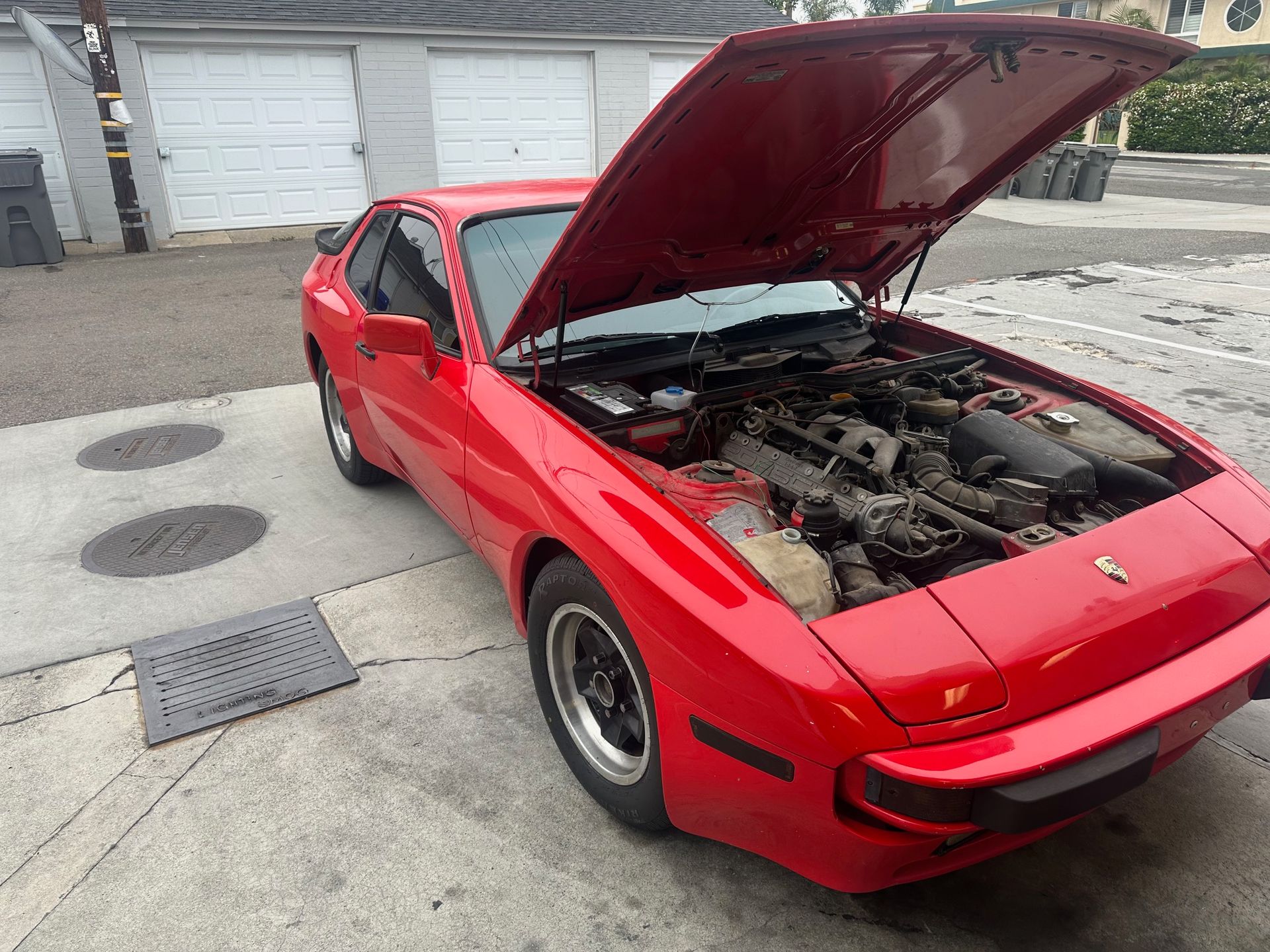 Red sports car with hood open in a driveway or parking area