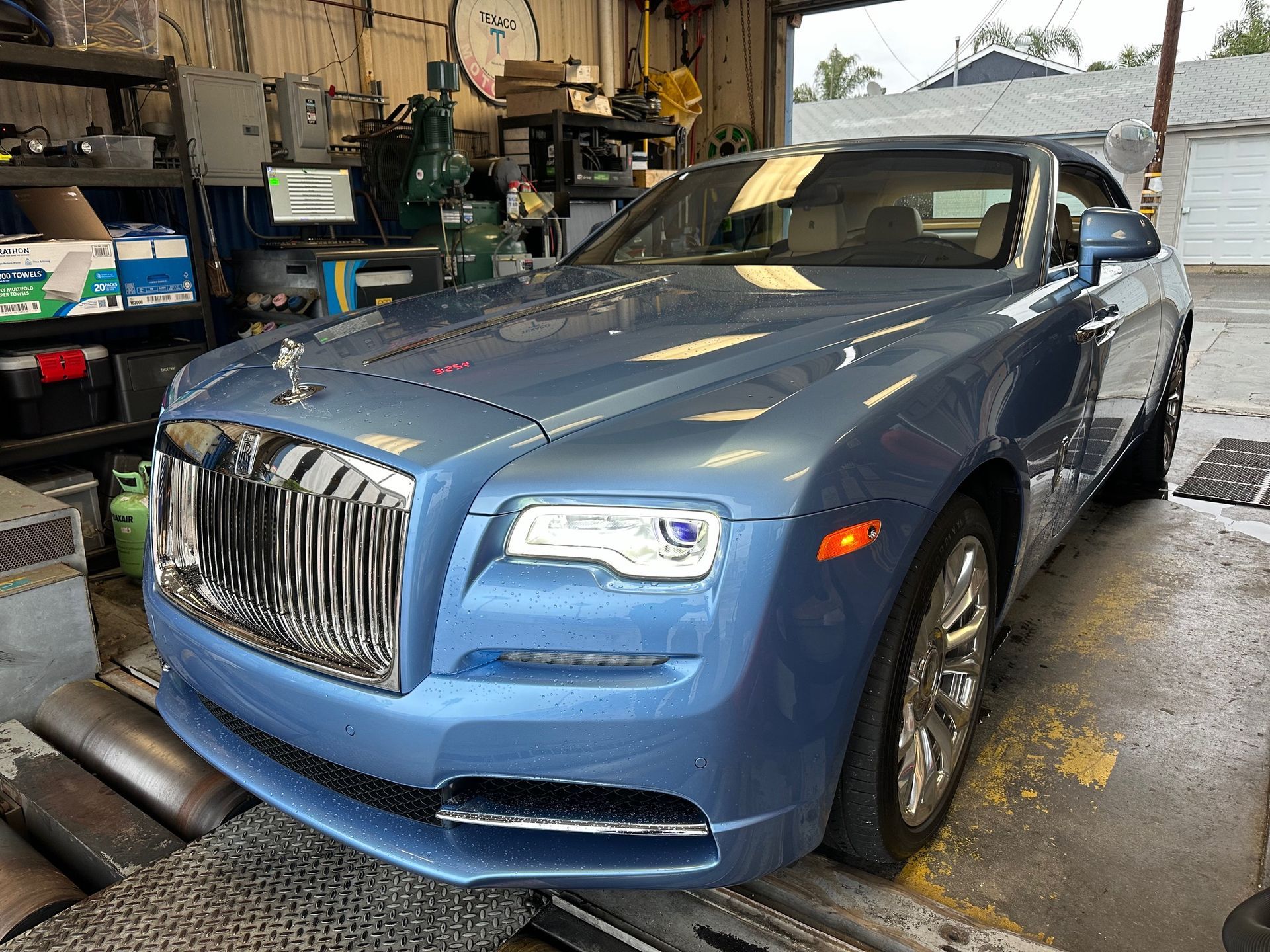 Blue Rolls-Royce in a garage, front view with chrome grille and headlights on.