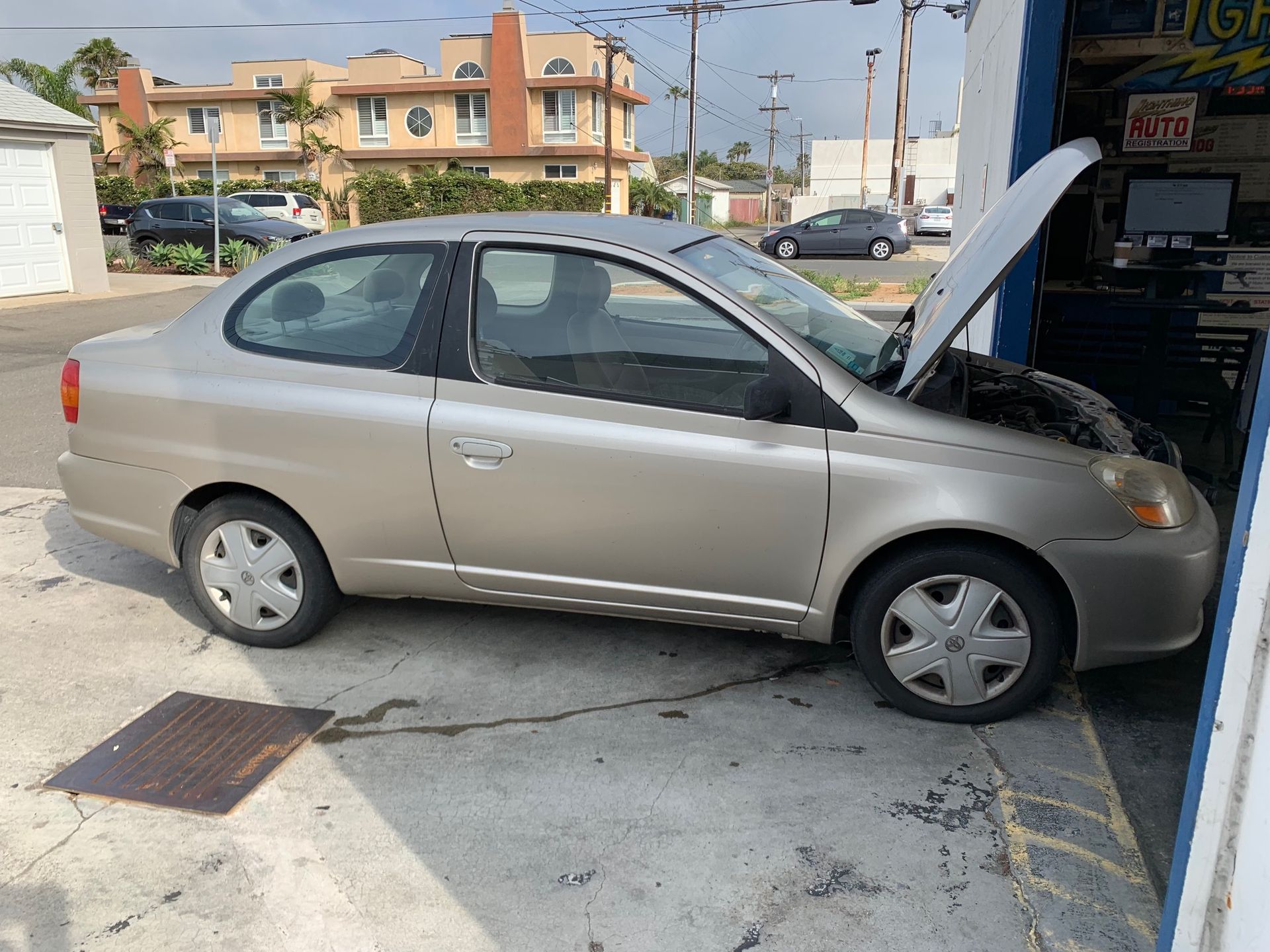 Tan sedan parked at a gas station with the hood open for repairs
