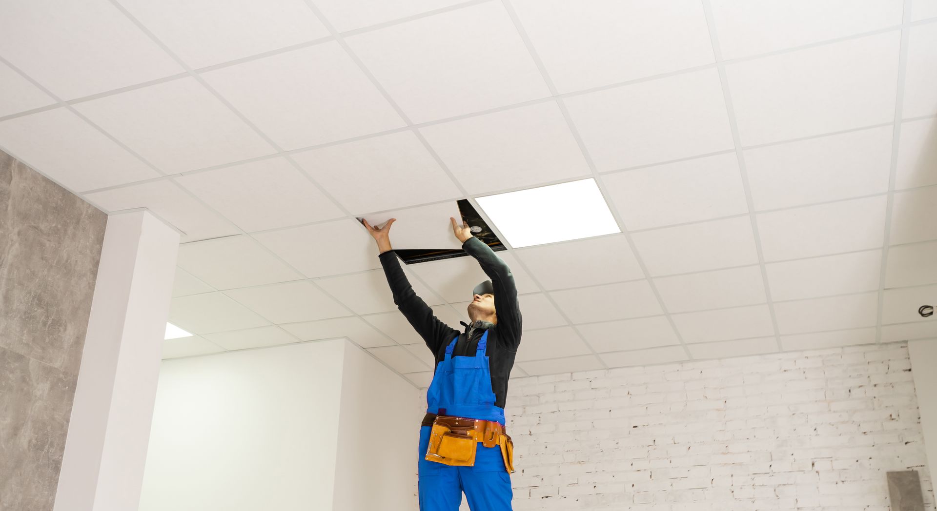 a man is hanging a light fixture from the ceiling .