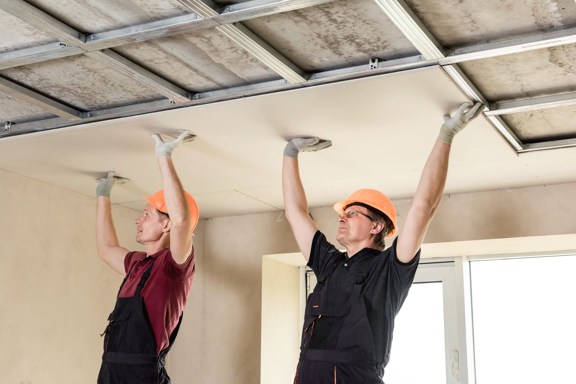 two men are working on a ceiling in a room .