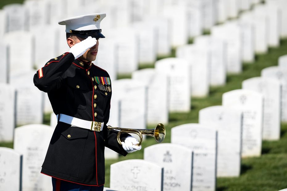 Marine saluting at a military cemetery beside rows of white gravestones