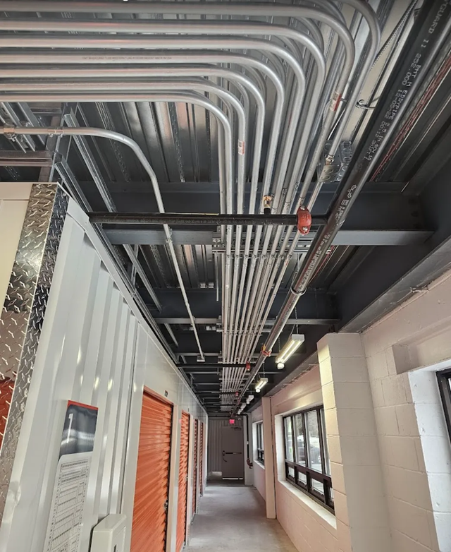 An indoor hallway in a storage facility with exposed silver conduit pipes running along the ceiling.