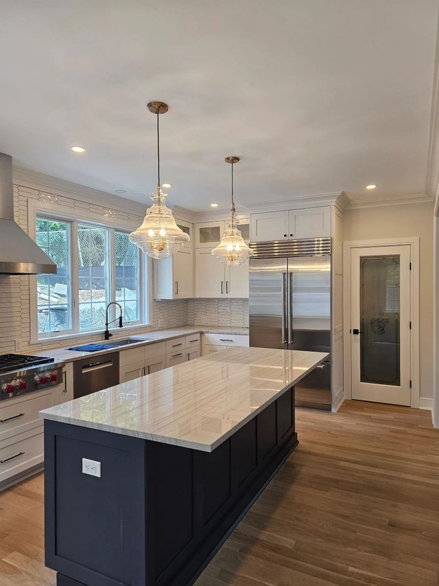 A modern kitchen with a dark blue island, white cabinets, stainless steel appliances, and two hanging pendant lights.