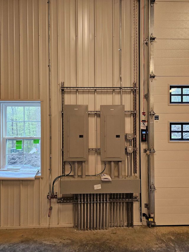 Two gray electrical panels mounted on a metal strut system against a white wall in an industrial garage setting.