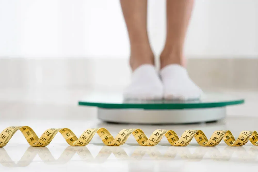 A woman is standing on a scale next to a measuring tape.
