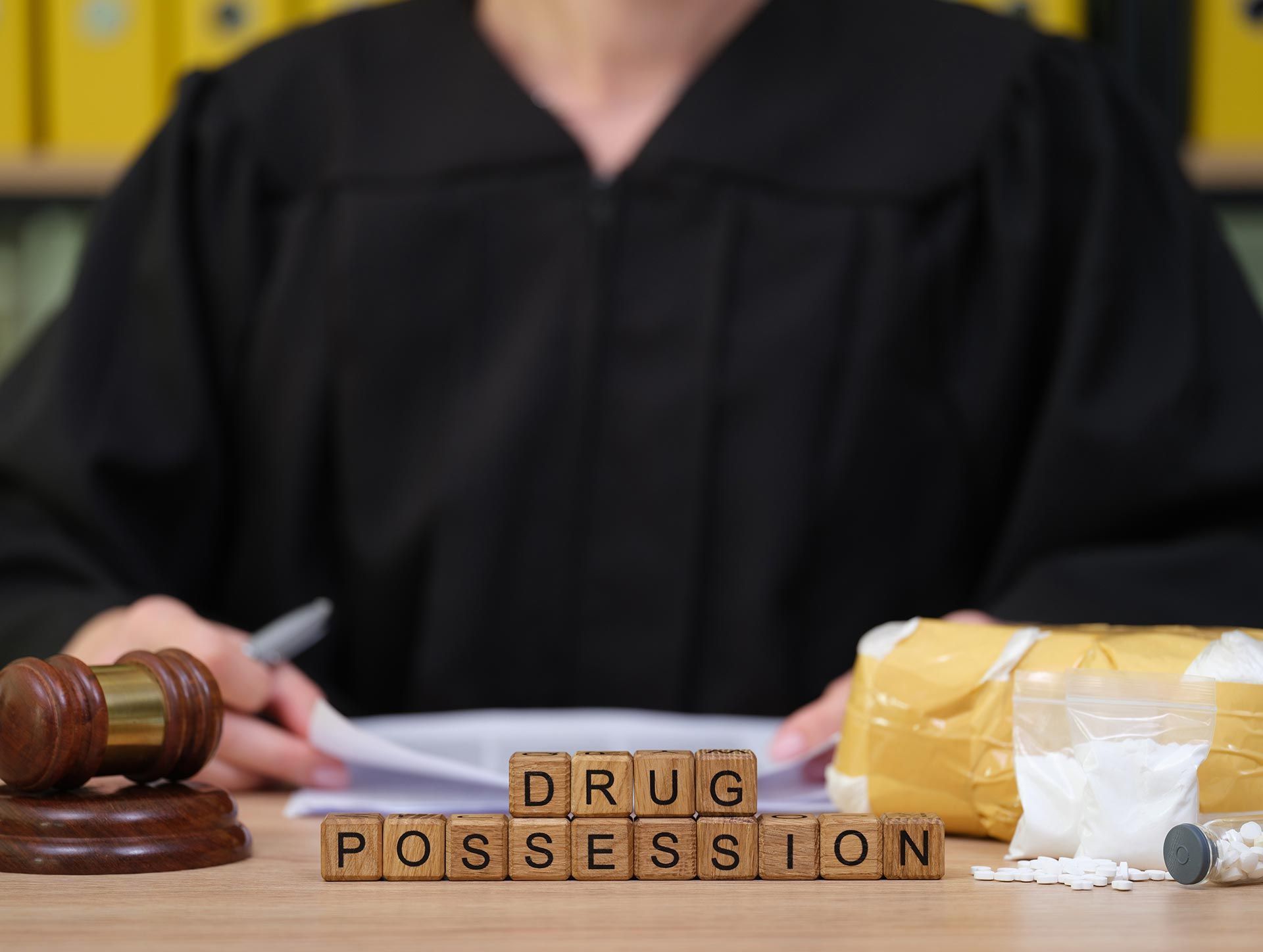 Judge’s gavel beside DRUG POSSESSION blocks and a bag of pills on a courtroom table Judge’s gavel beside DRUG POSSESSION blocks and a bag of pills on a courtroom table