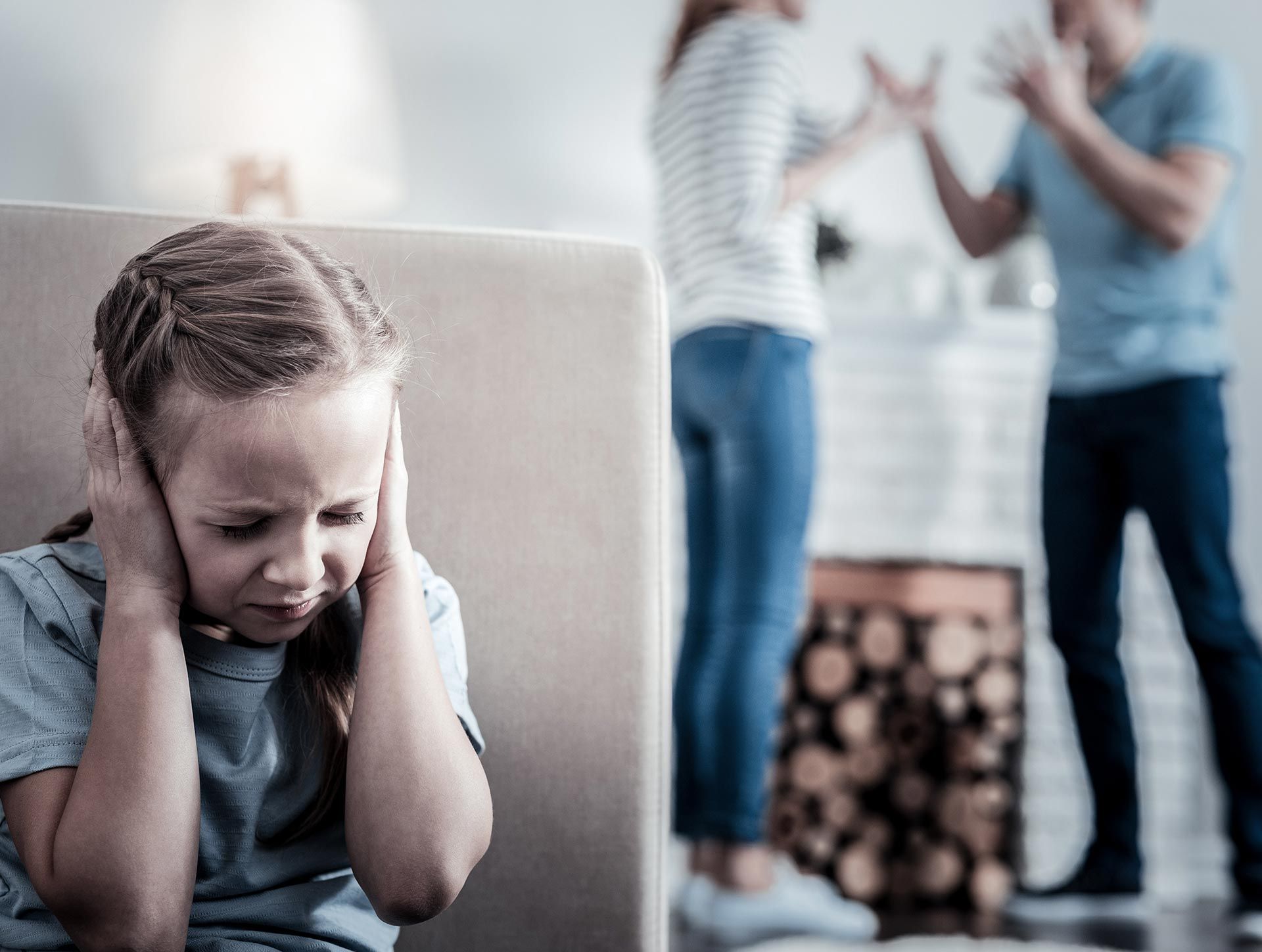 Distressed child covering ears while adults argue in the blurred background Distressed child covering ears while adults argue in the blurred background