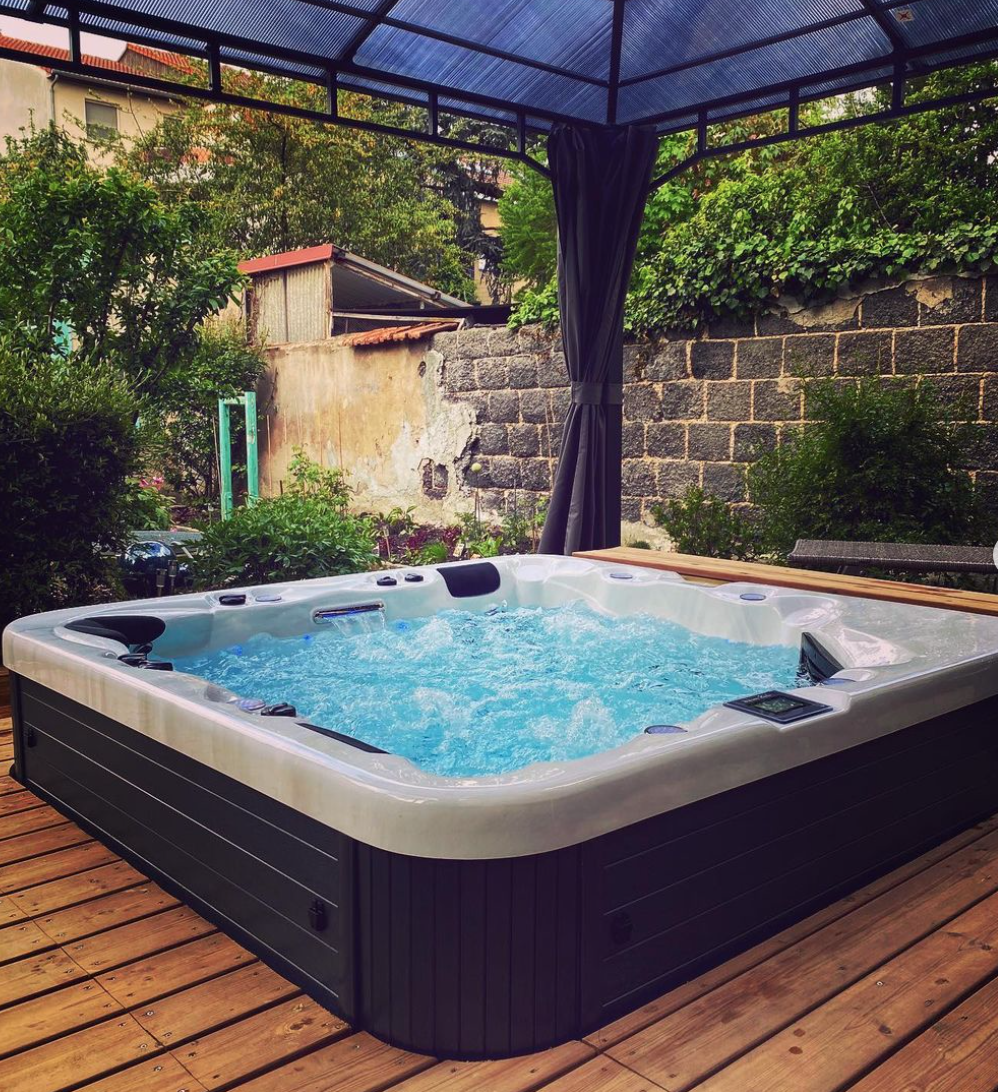 Un grand bain à remous est installé sur une terrasse en bois sous un auvent.