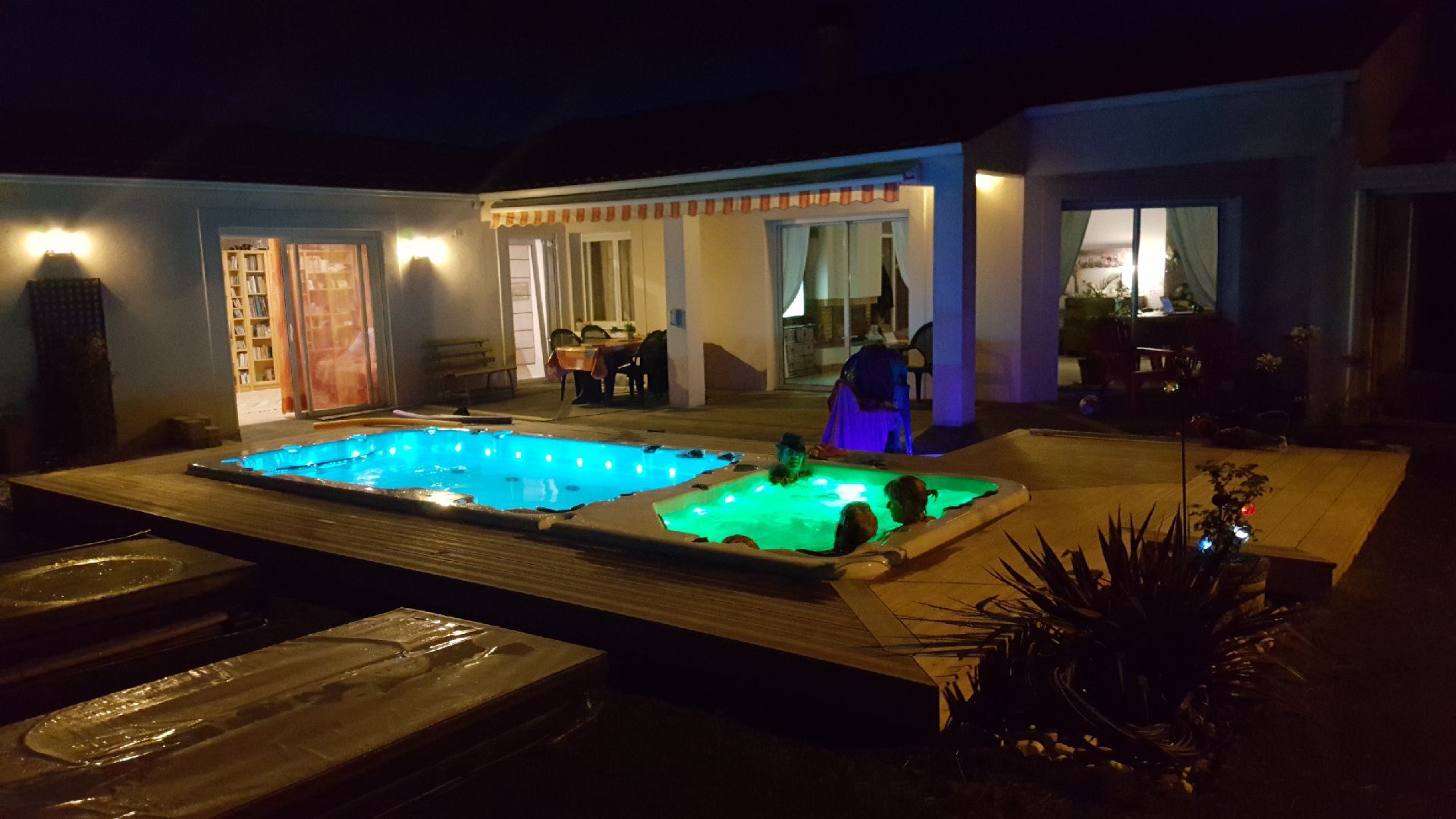 Un couple de personnes est assis dans un jacuzzi devant une maison la nuit.
