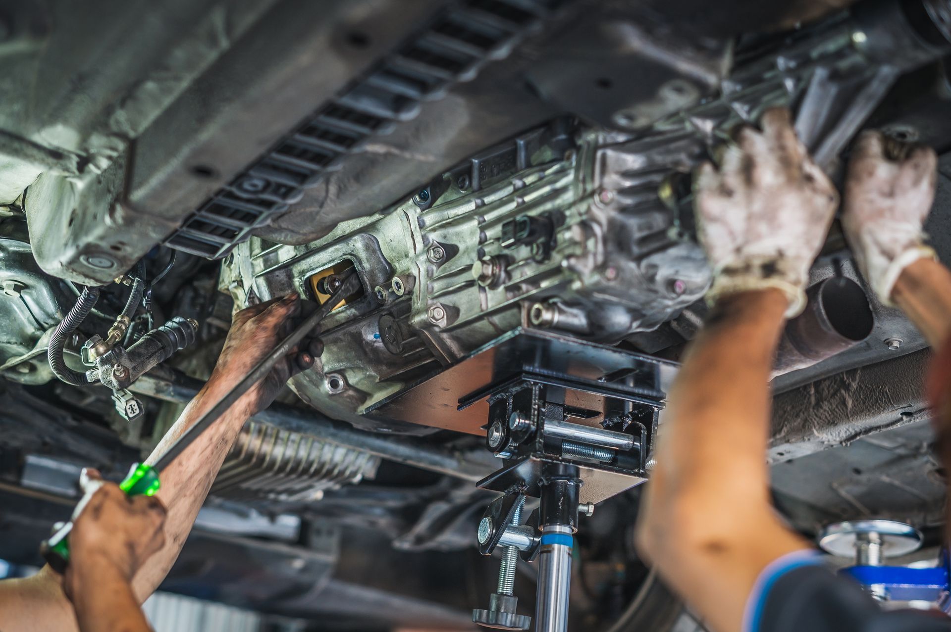 Mechanic using a wrench to service a vehicle's transmission from below. Mechanic using a wrench to service a vehicle's transmission from below.