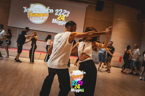 Una coppia balla stretta in uno studio con altri ballerini sullo sfondo.