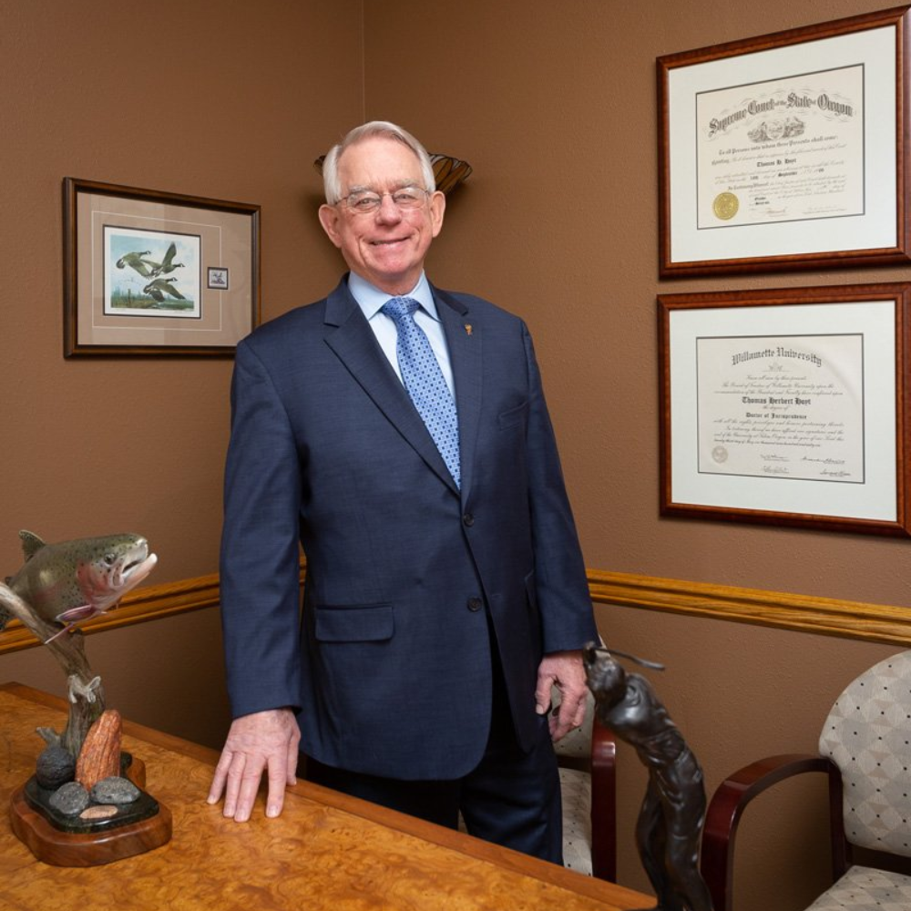 Man in suit stands in an office with diplomas, a sculpture, and artwork.