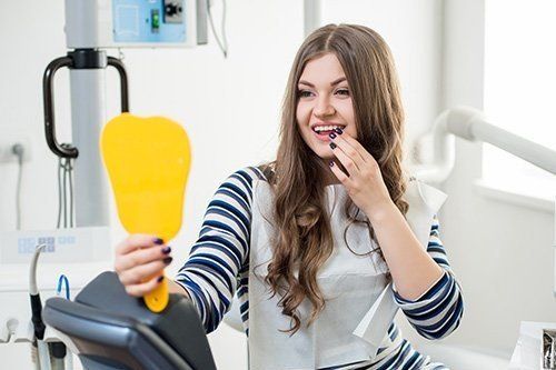 a woman is looking at her teeth in a mirror at the dentist .