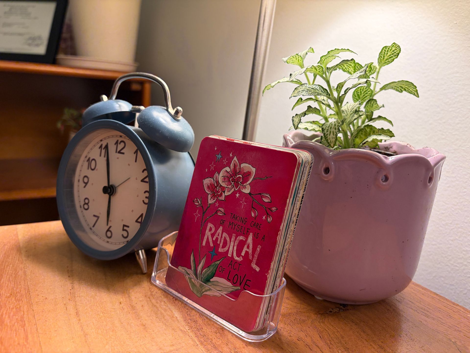 Blue alarm clock, pink potted plant, and journal arranged on a therapist’s office desk