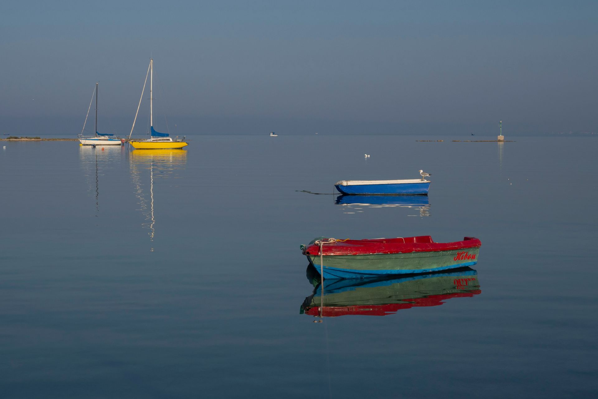 Small sailboats and a red-blue dinghy floating on calm blue water at dusk