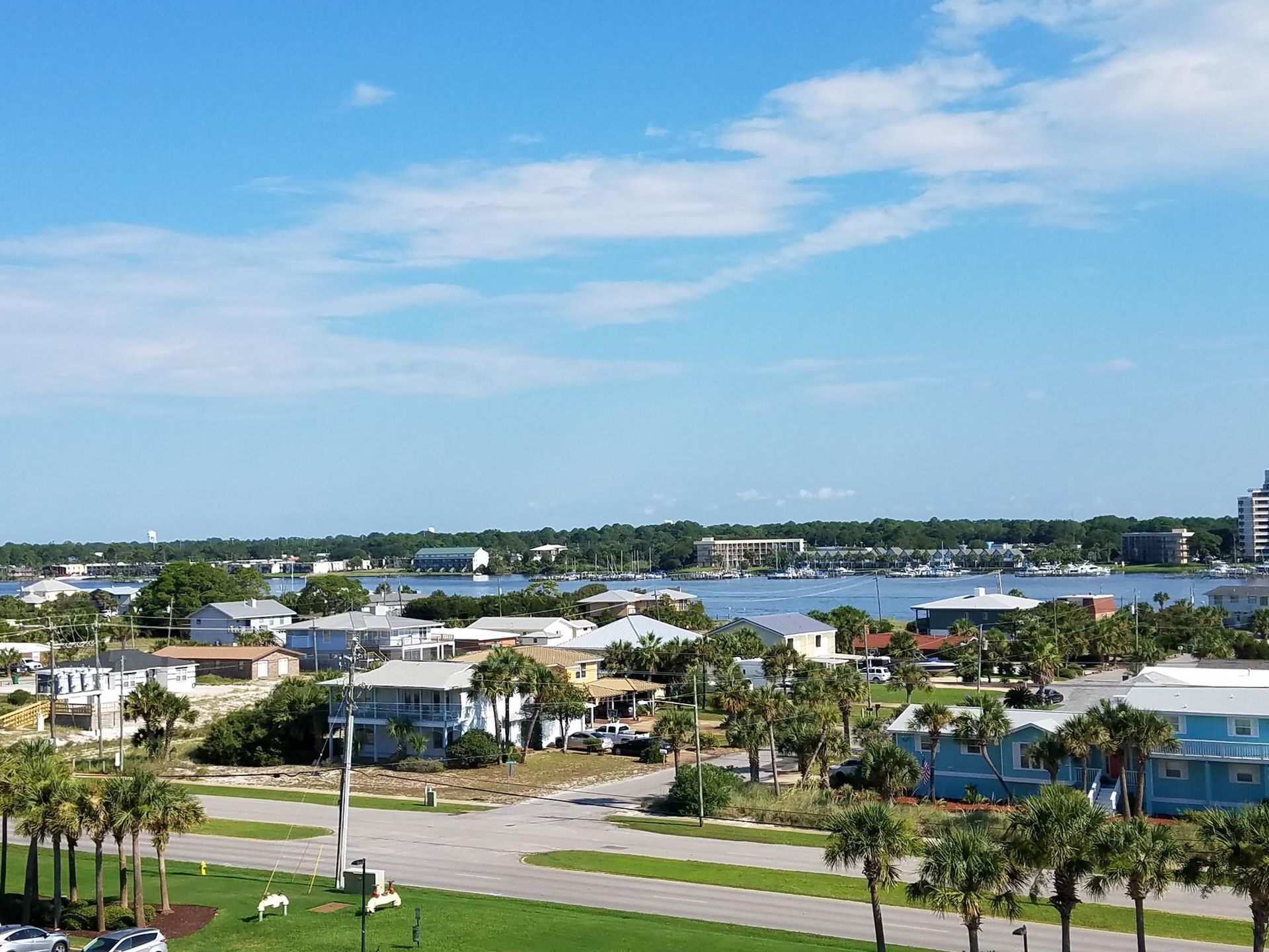 Coastal neighborhood with palm trees, houses, roads, and blue water under a clear sky