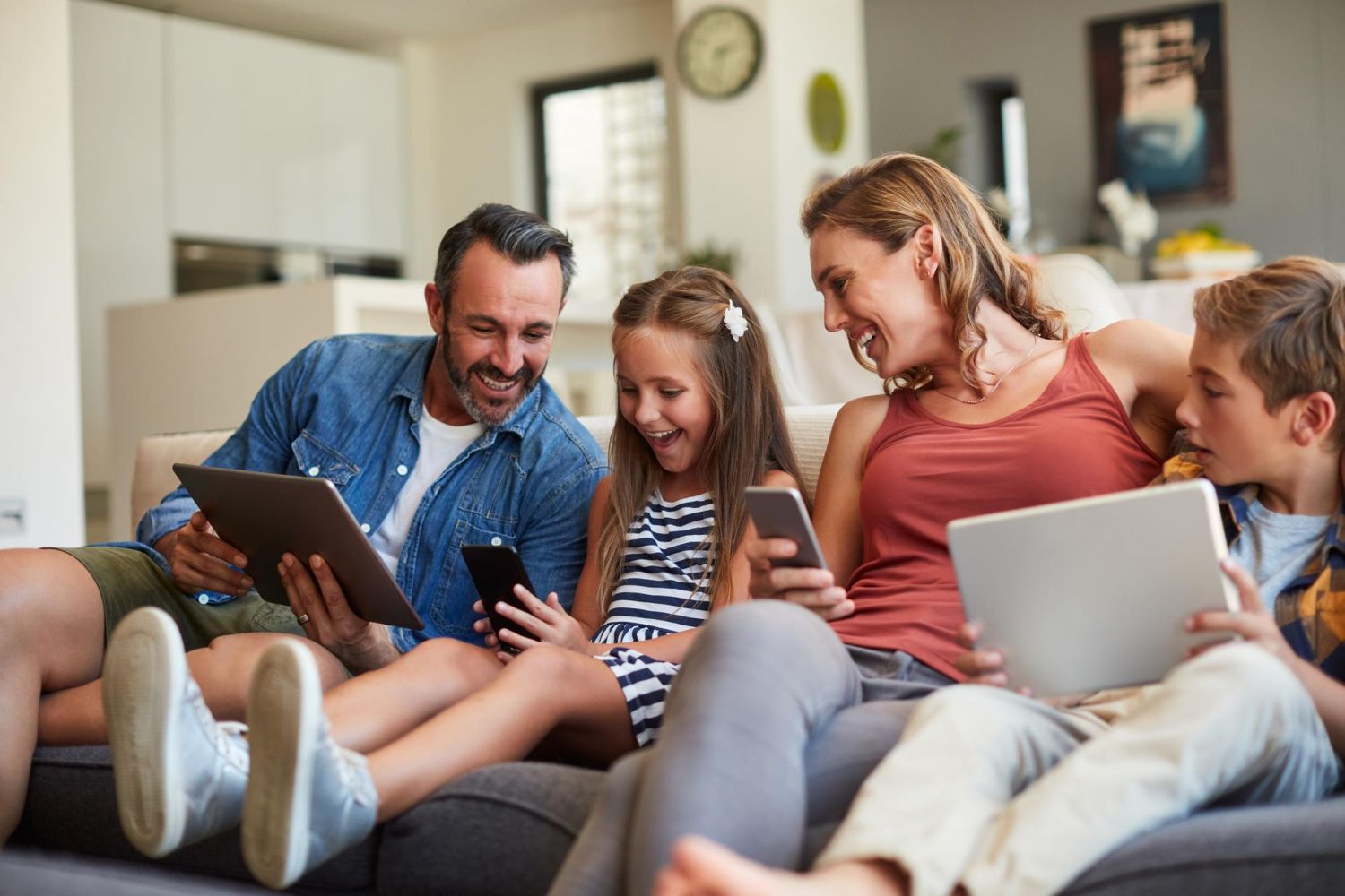 Family sitting on a couch using a tablet and laptop in a cozy living room