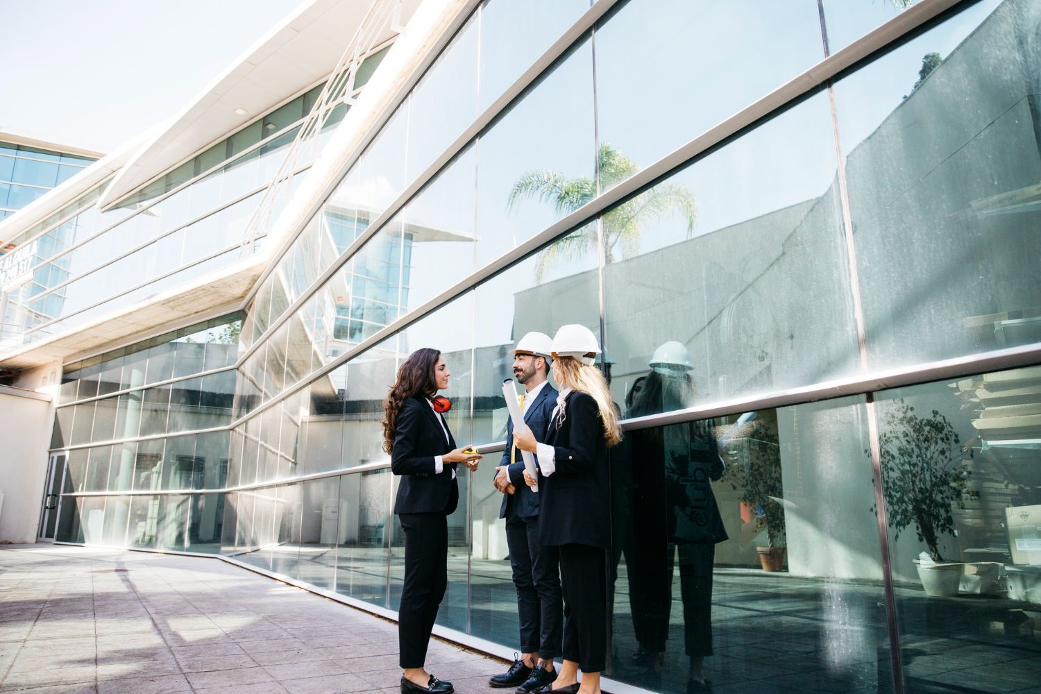Two professionals in hard hats discussing by a glass building exterior.