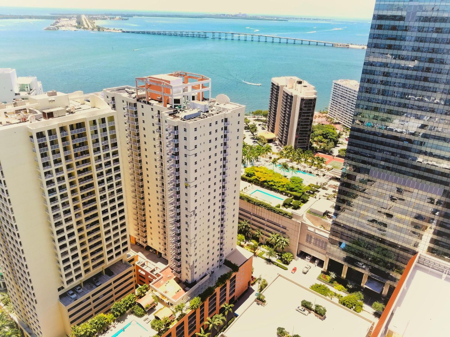 High-rise waterfront city skyline with turquoise bay and distant bridge under a bright sky