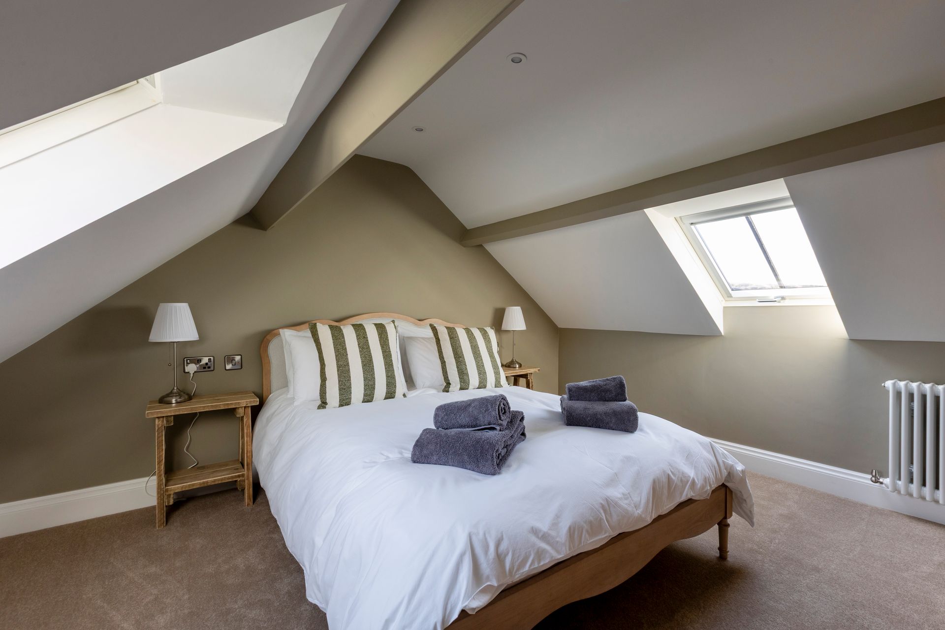 Cozy attic bedroom with white bed, striped pillows, bedside table, and sloped windows