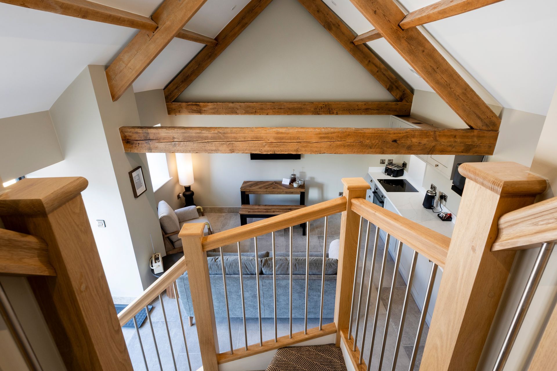Loft stair landing with wooden beams, white walls, and a small seating area below