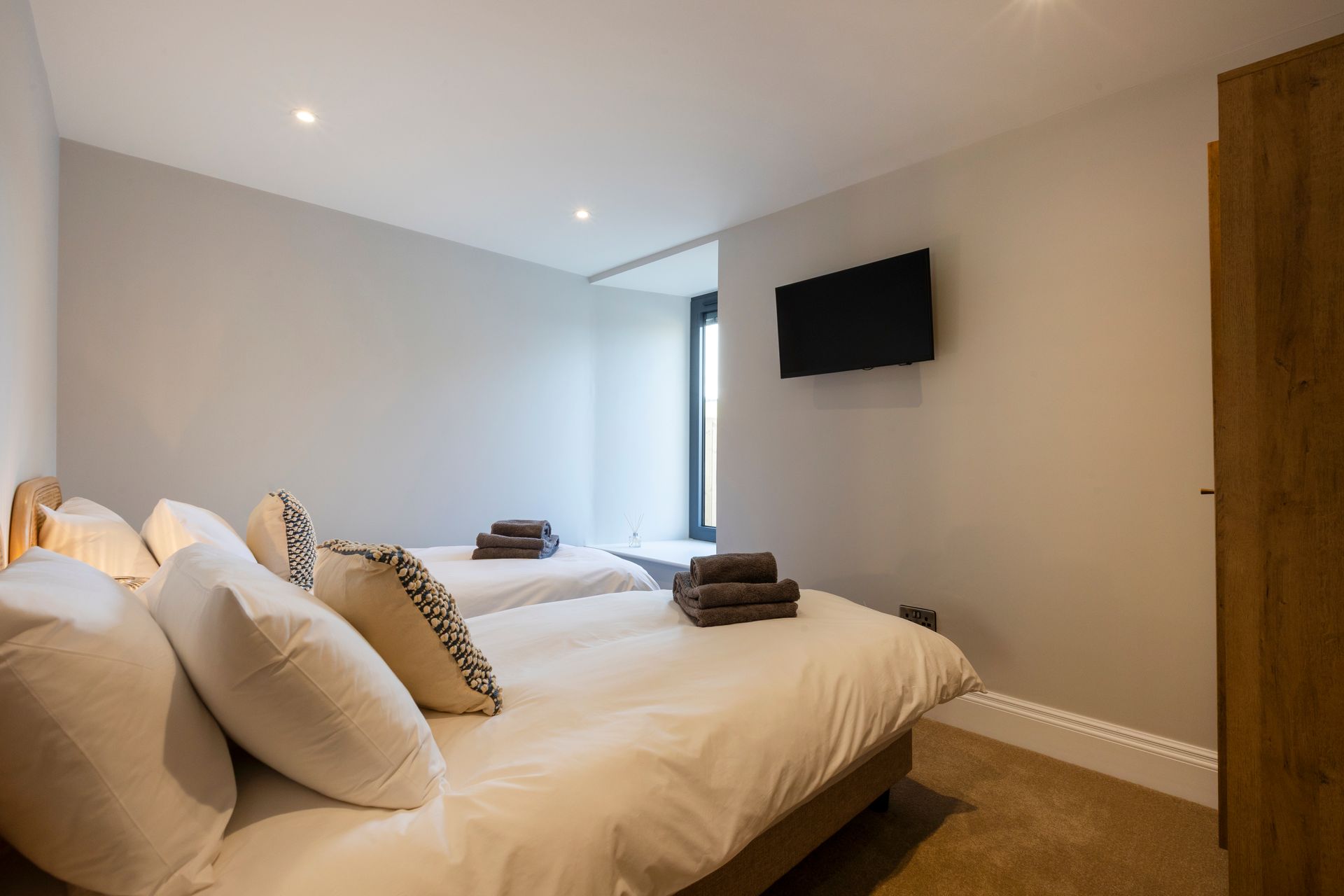 Bedroom with two beds, white bedding, wall-mounted TV, and neutral decor.