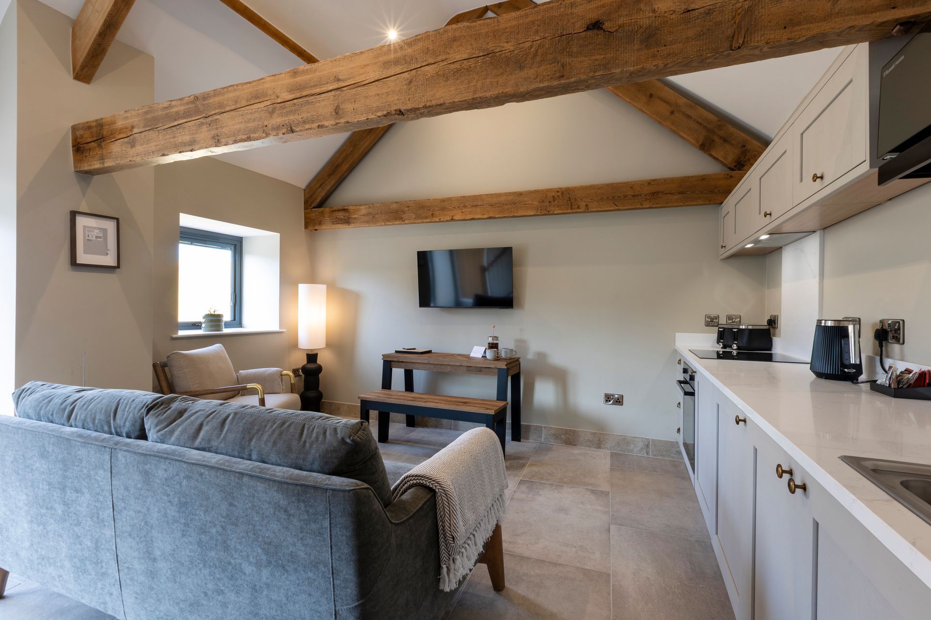 Cozy living room with exposed wood beams, gray sofa, TV, desk, and white cabinets in the background