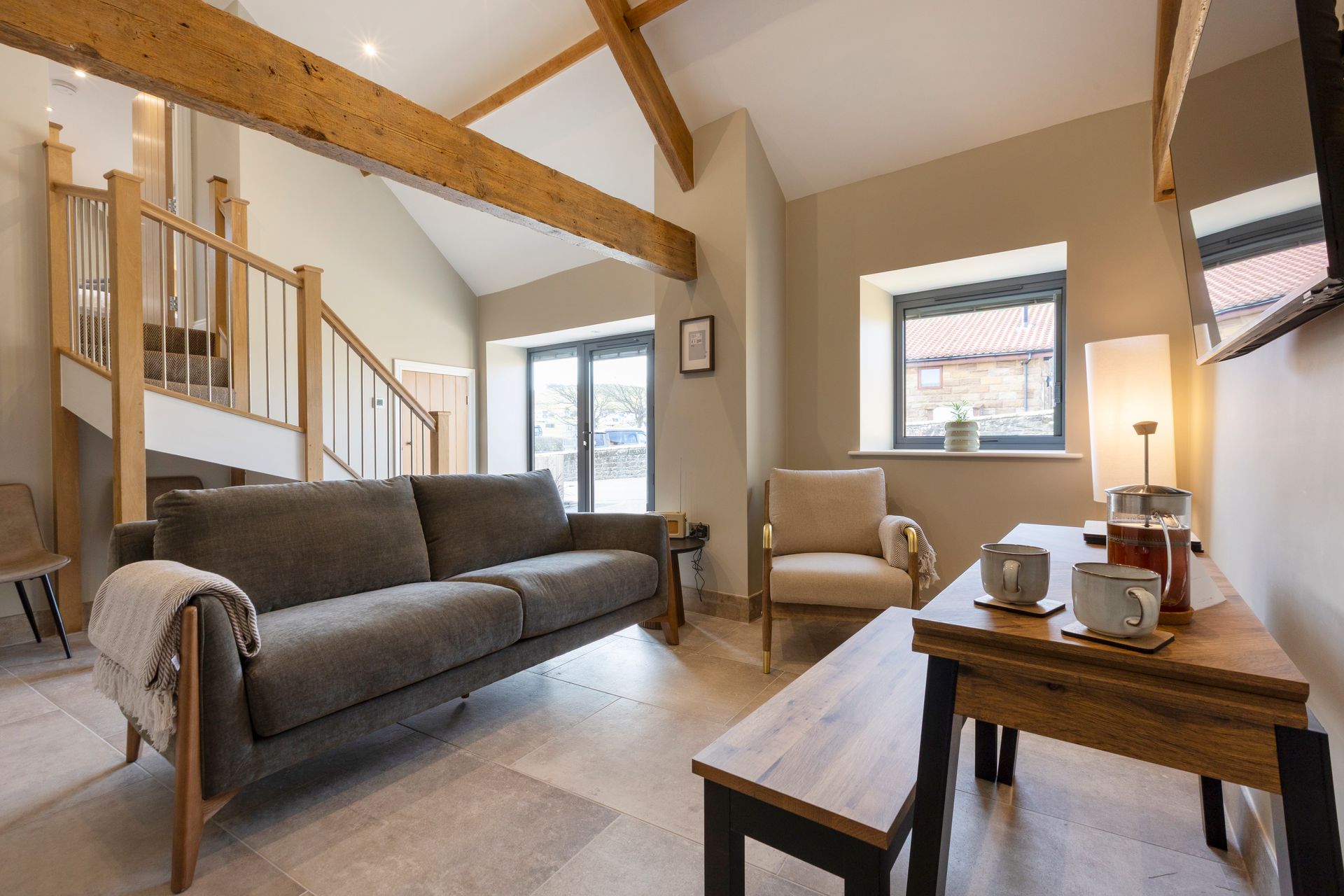 Bright living room with gray sofa, wooden beams, and coffee table by the window