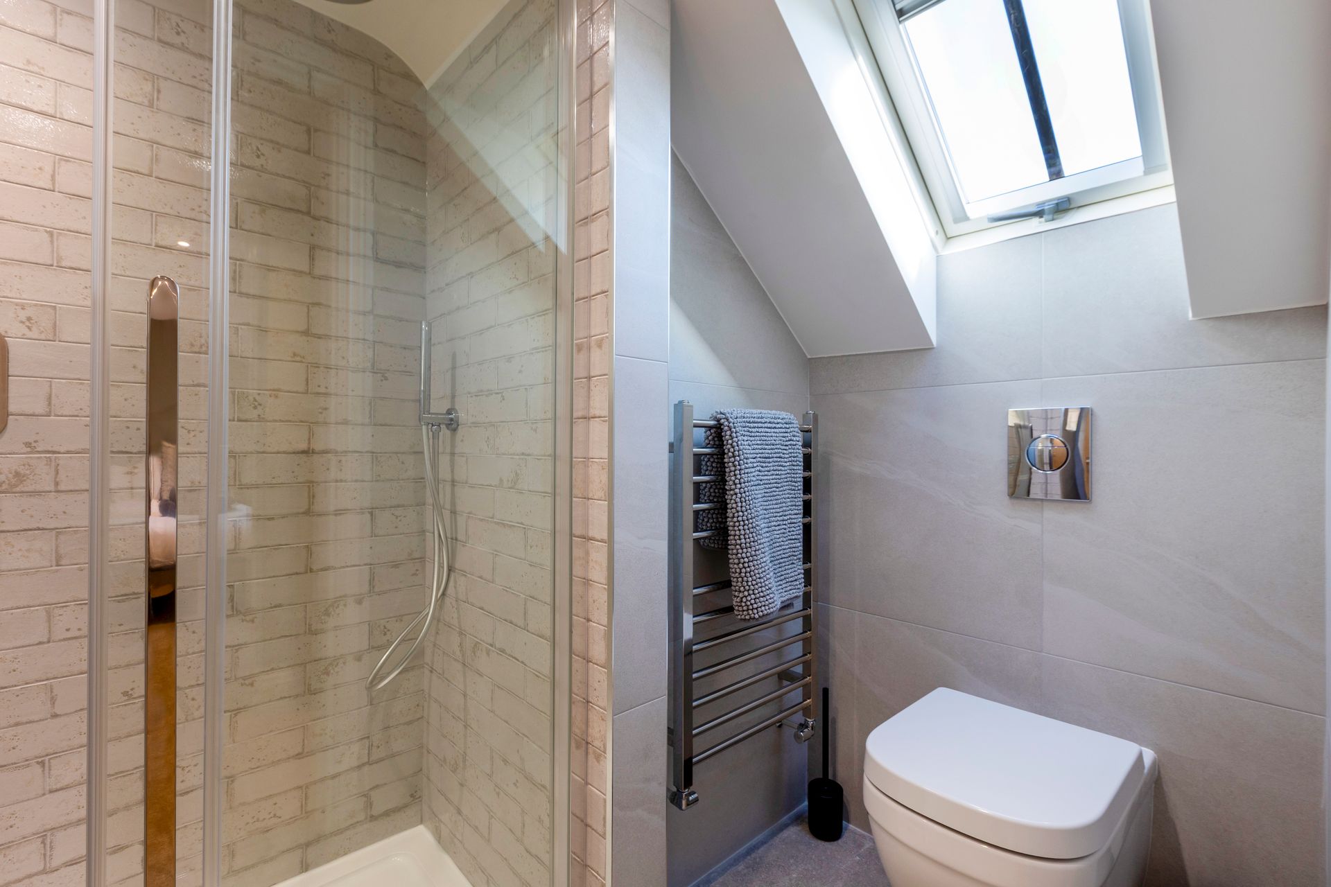 Modern bathroom with glass shower, white tiled walls, towel rack, and skylight over the toilet