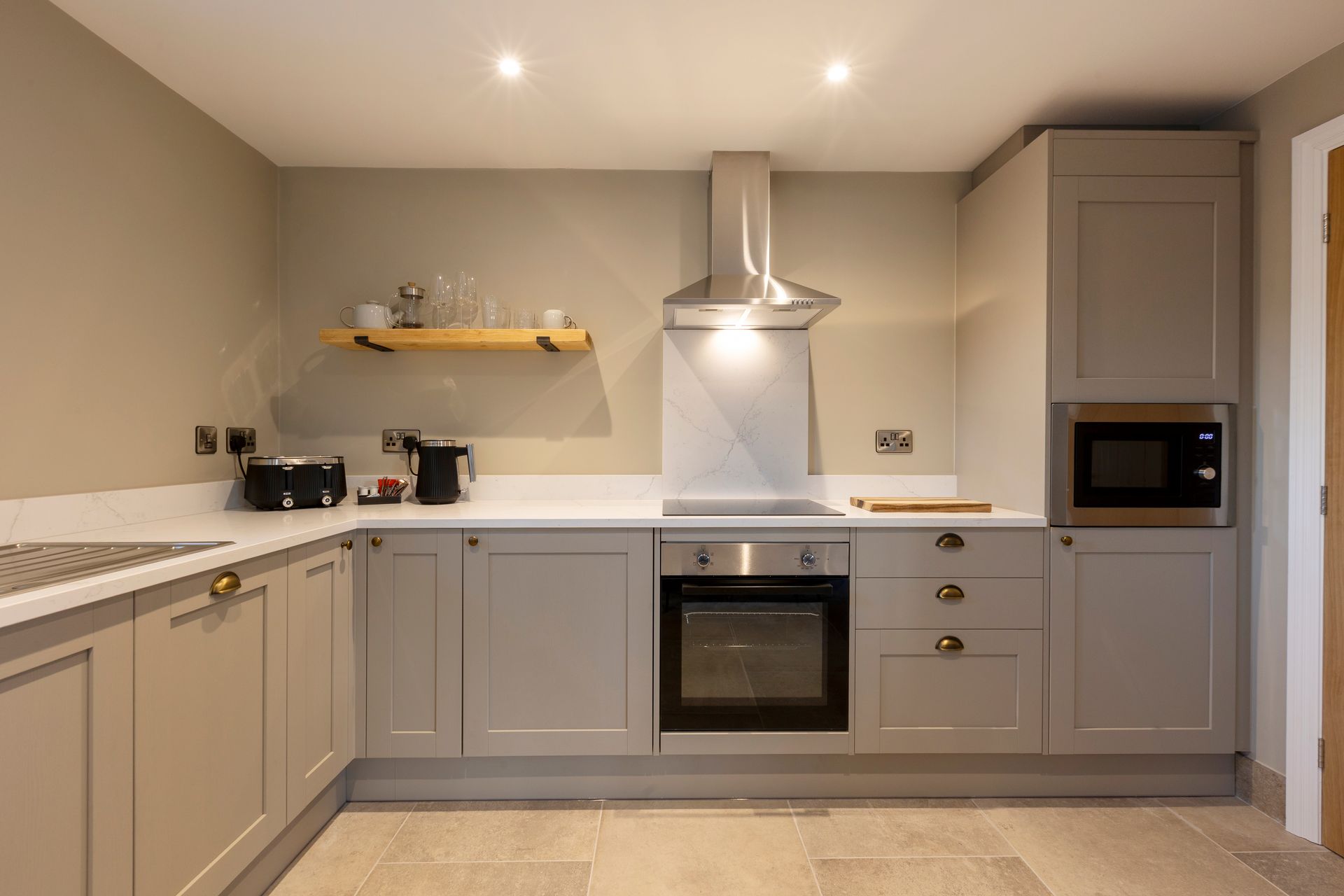 Modern gray kitchen with white countertops, built-in oven, range hood, and wall-mounted shelf